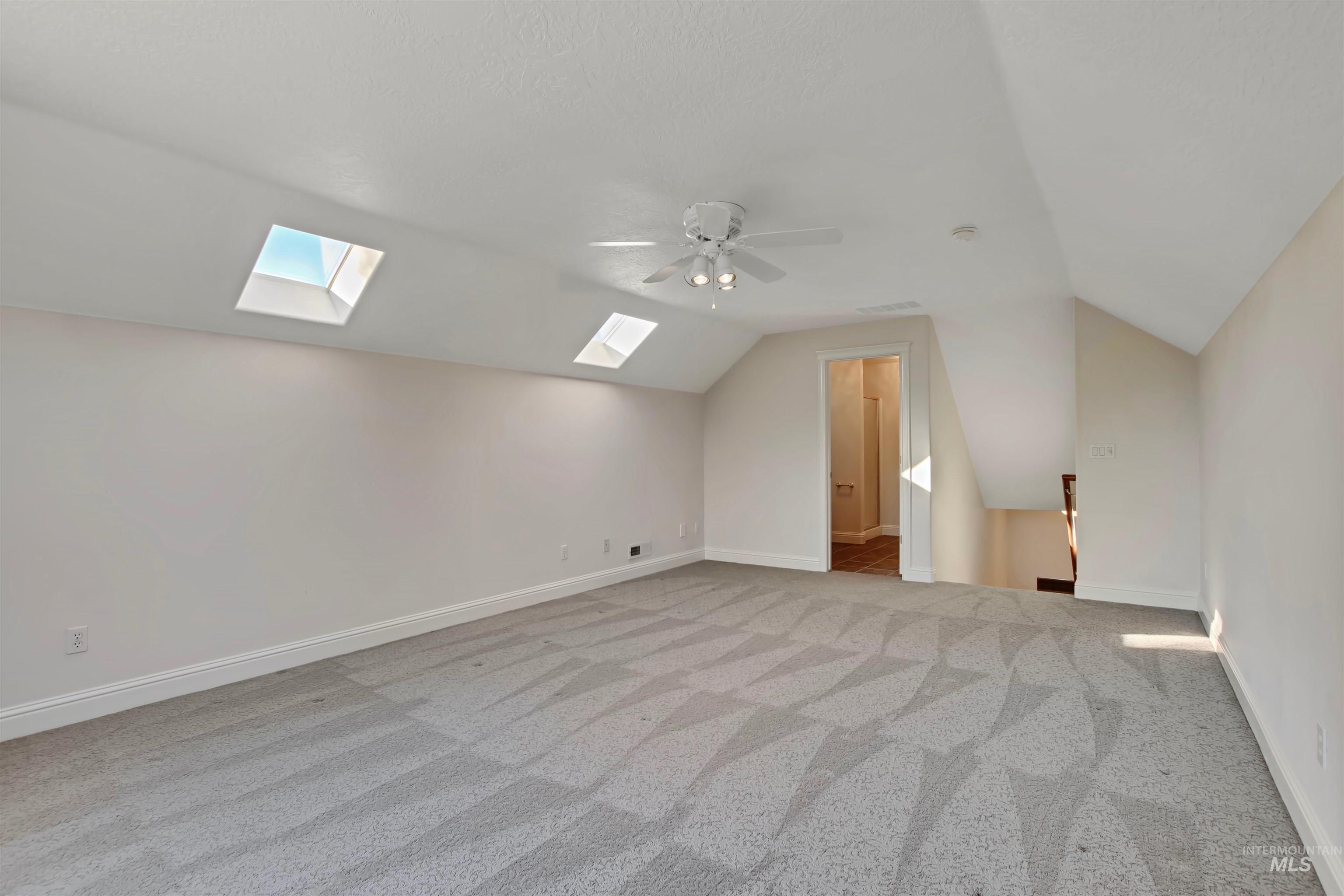 Bonus room with light carpet, a skylight, lofted ceiling, and ceiling fan