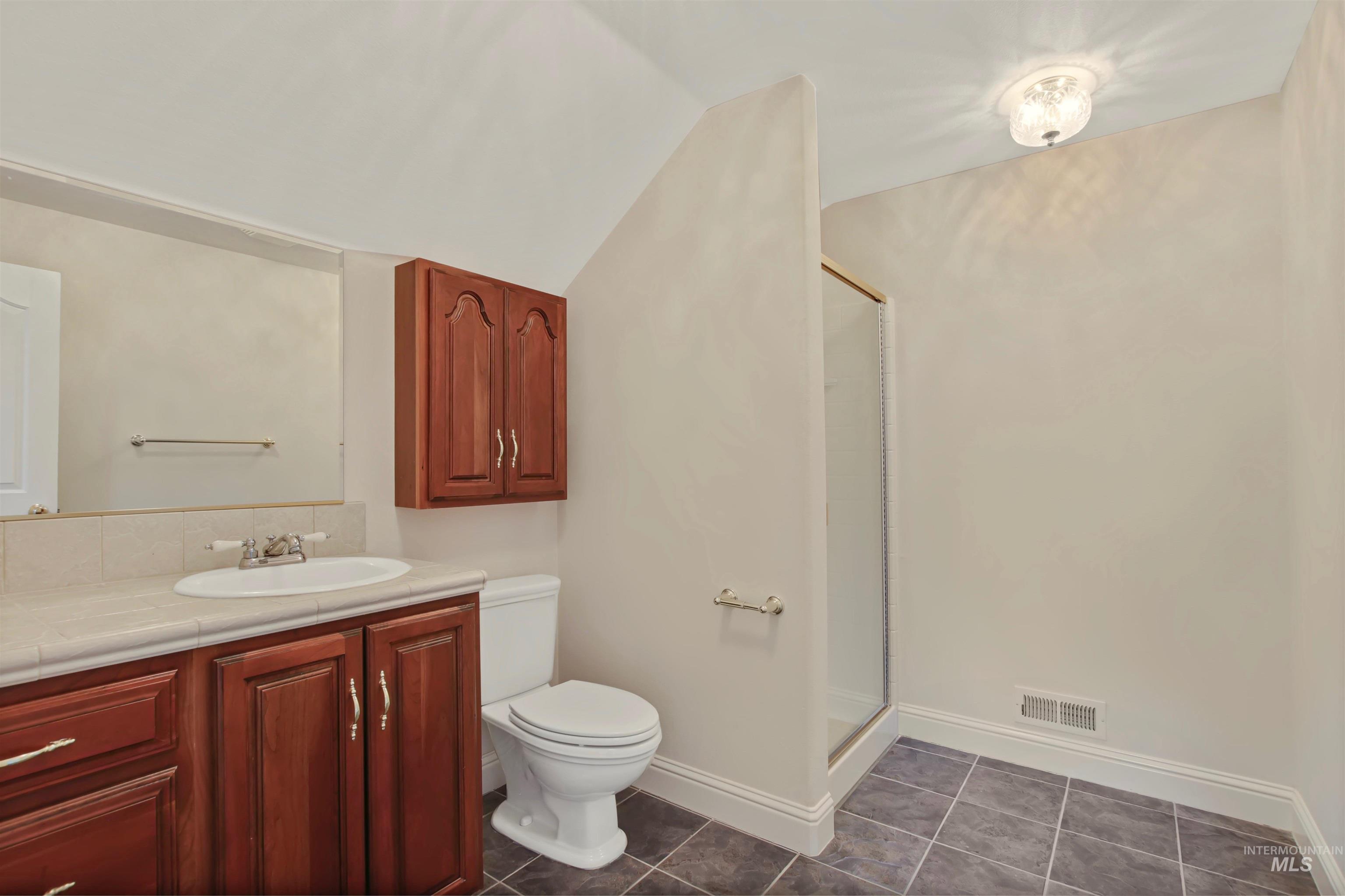 Full bathroom with vaulted ceiling, vanity, a stall shower, and dark tile patterned flooring