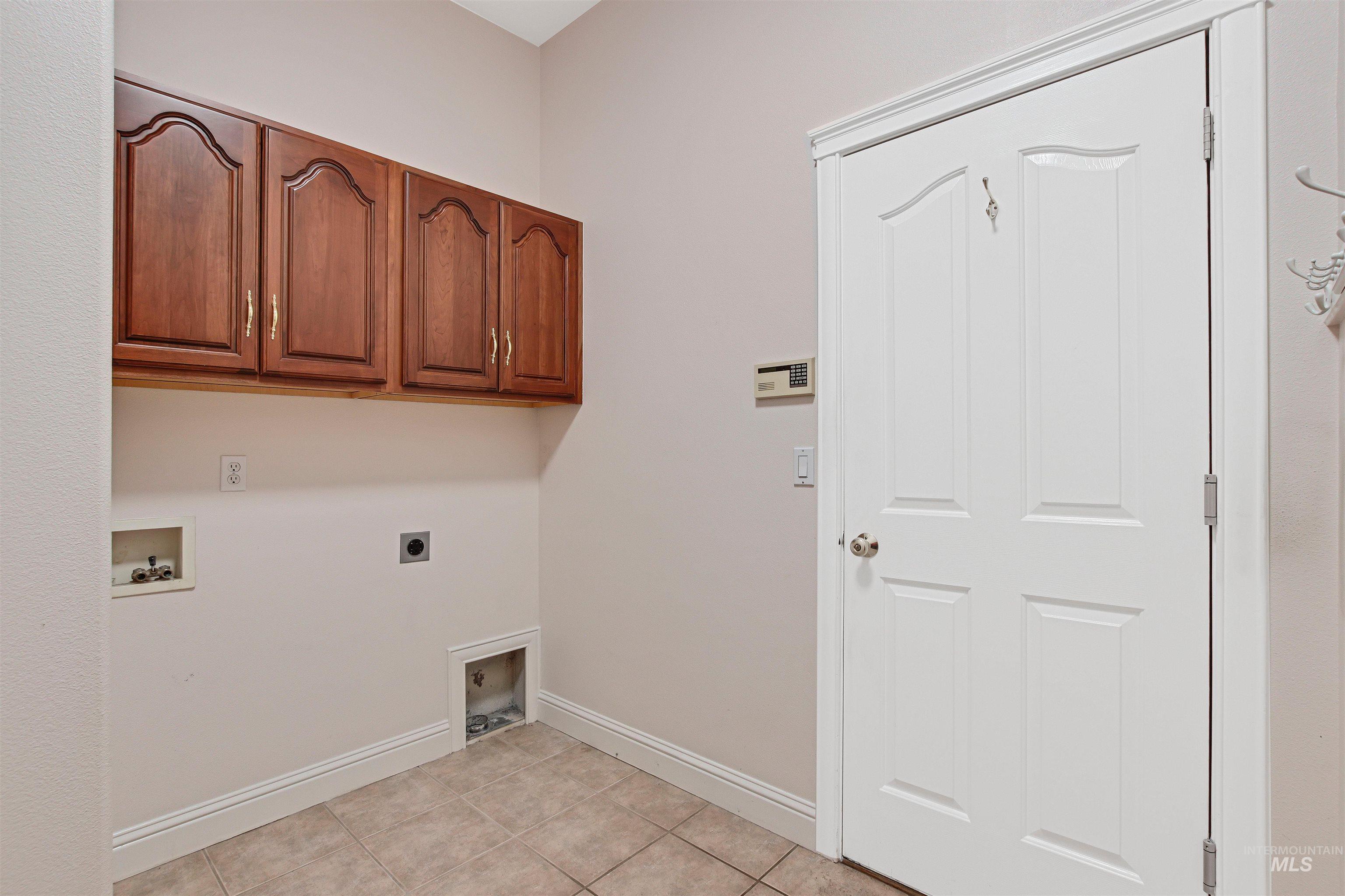 Laundry area with hookup for a washing machine, electric dryer hookup, cabinet space, and light tile patterned floors