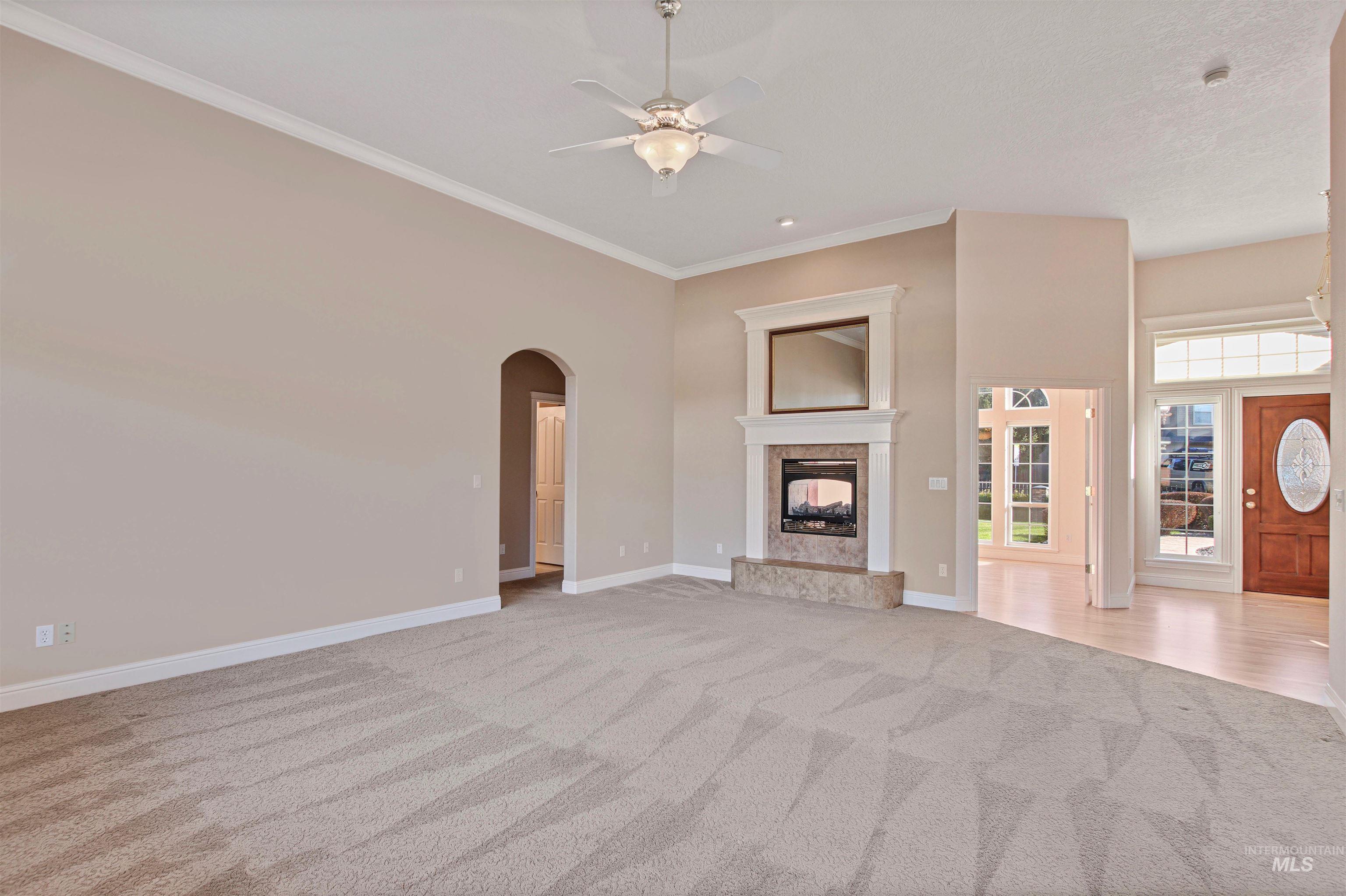 Unfurnished living room featuring light colored carpet, arched walkways, ornamental molding, a premium fireplace, and ceiling fan