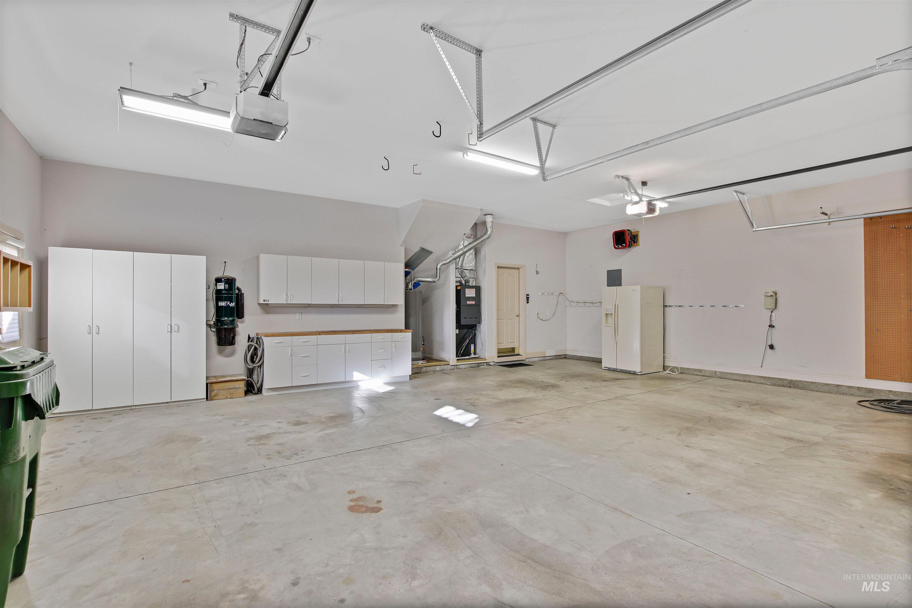 Garage featuring white refrigerator with ice dispenser, a garage door opener, and water heater
