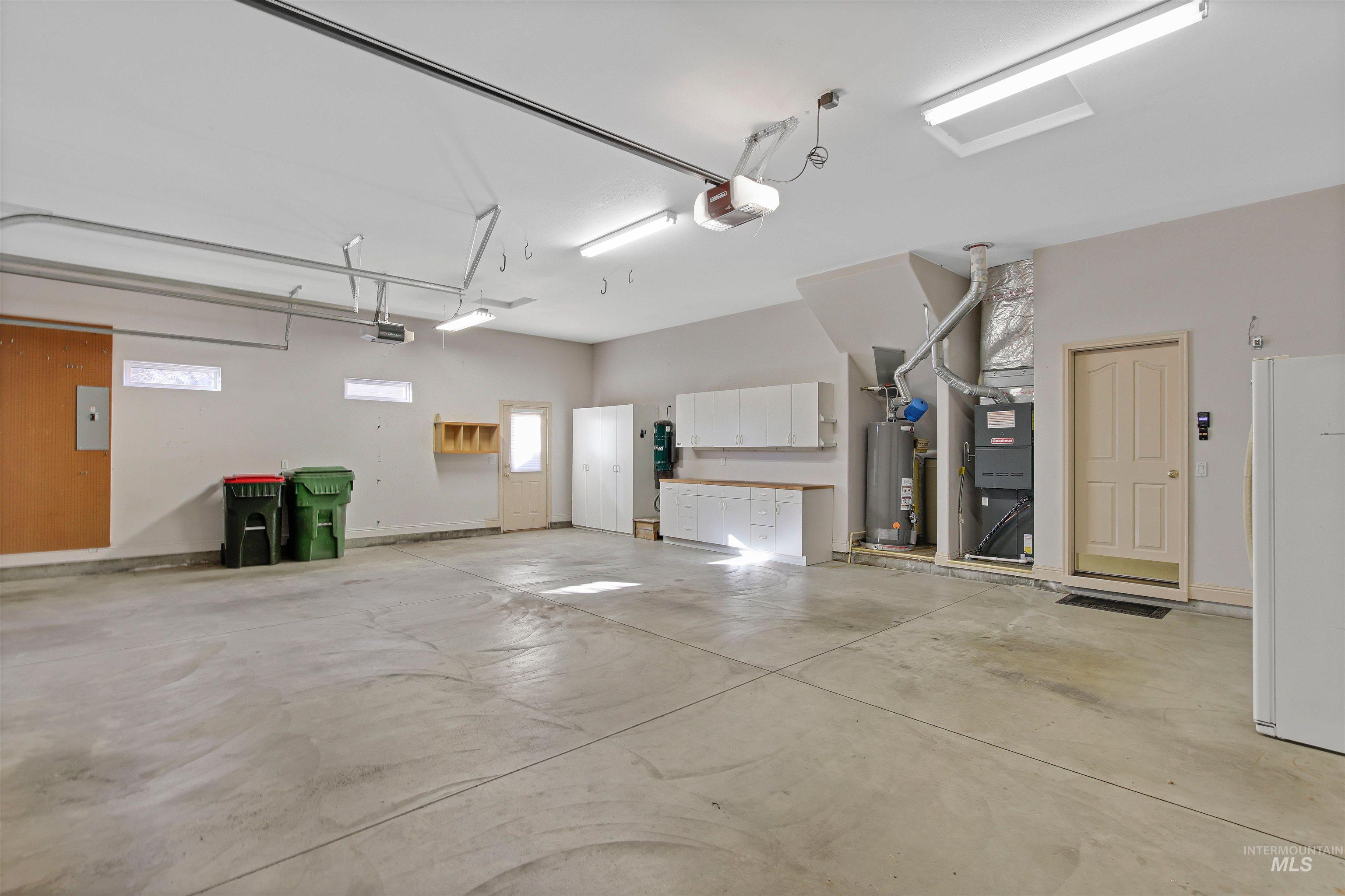 Garage with freestanding refrigerator, gas water heater, a garage door opener, and electric panel