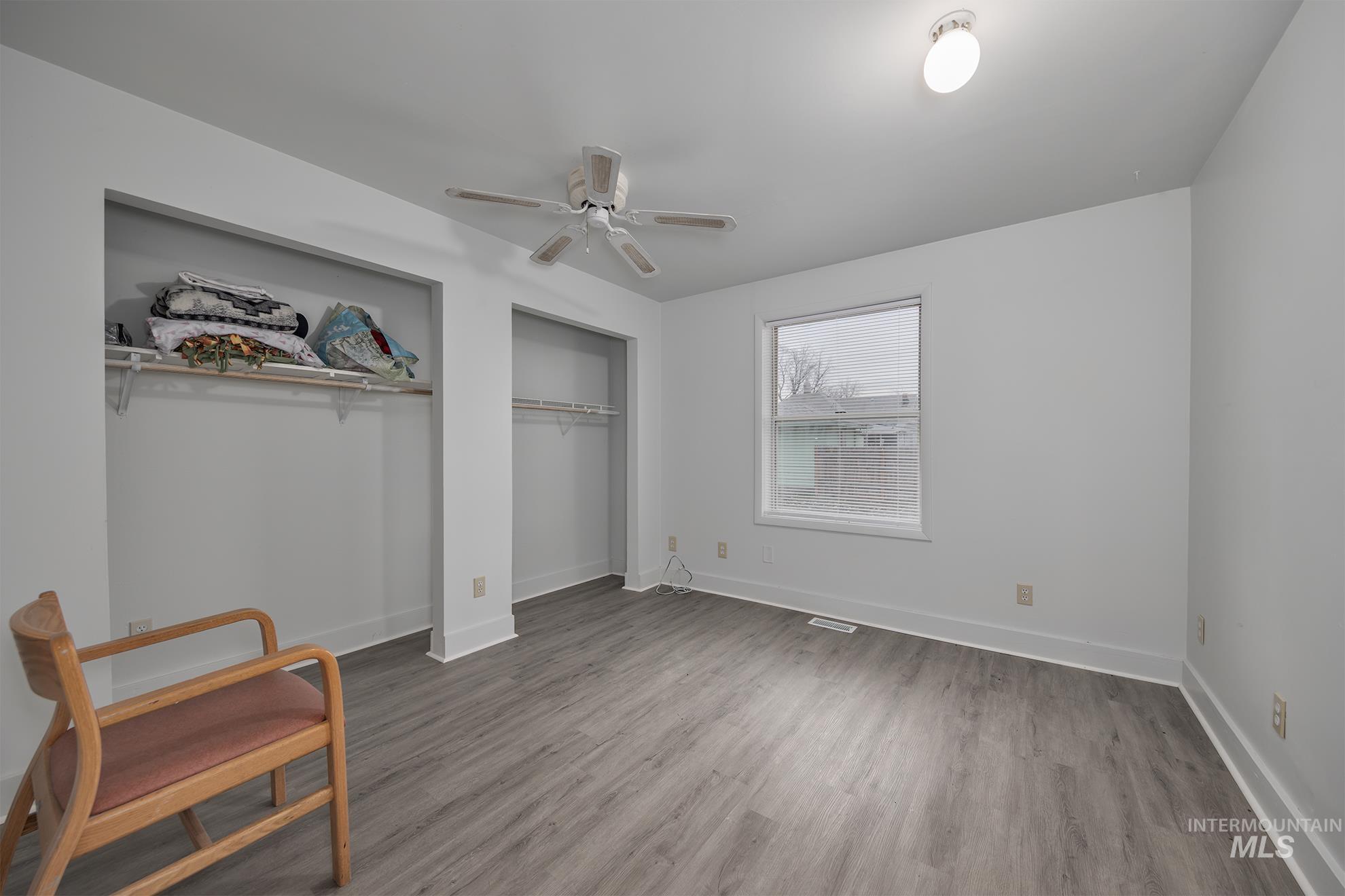 Unfurnished bedroom with a ceiling fan, light wood-style floors, and two closets