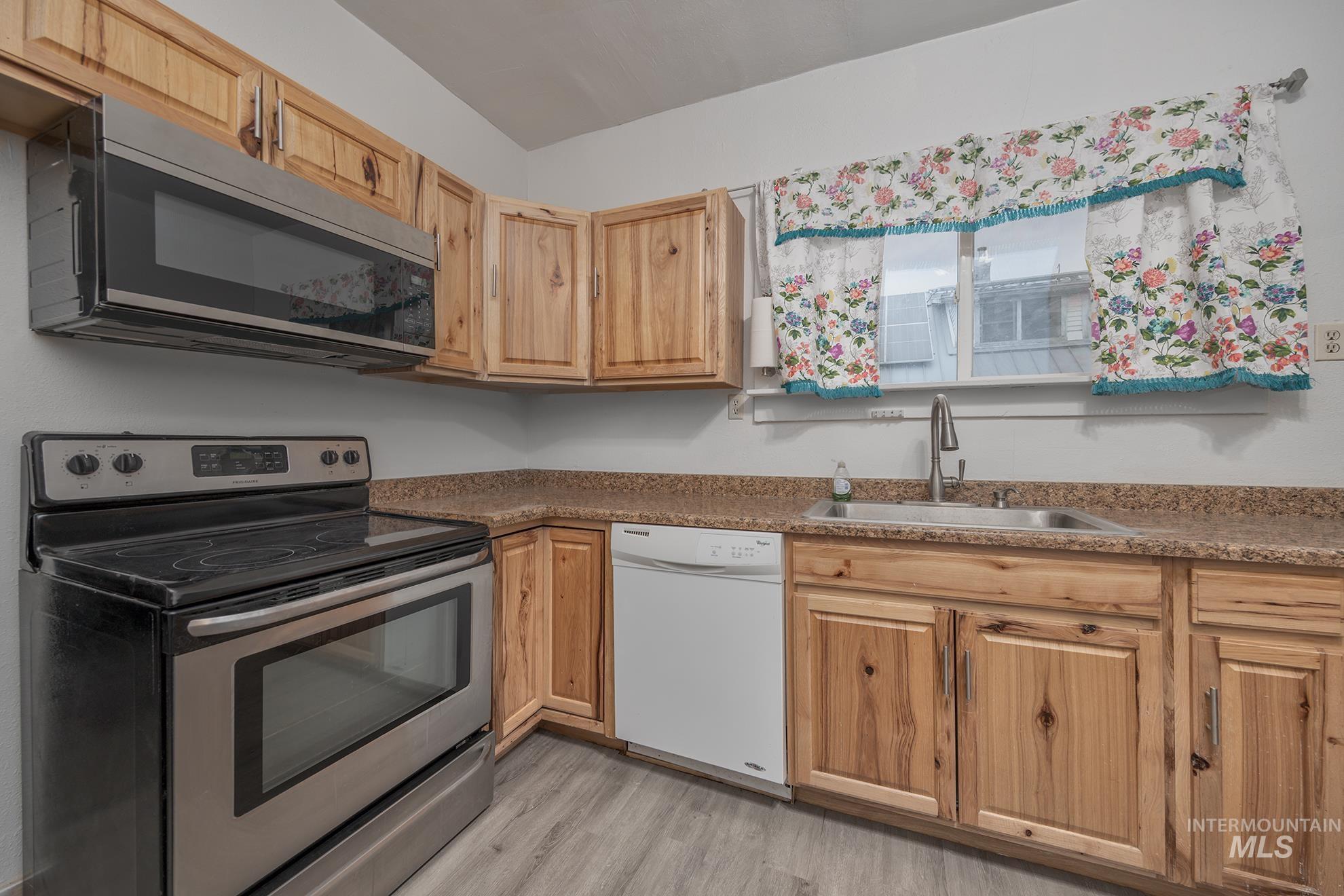 Kitchen with stainless steel appliances, light wood-style floors, and dark stone countertops