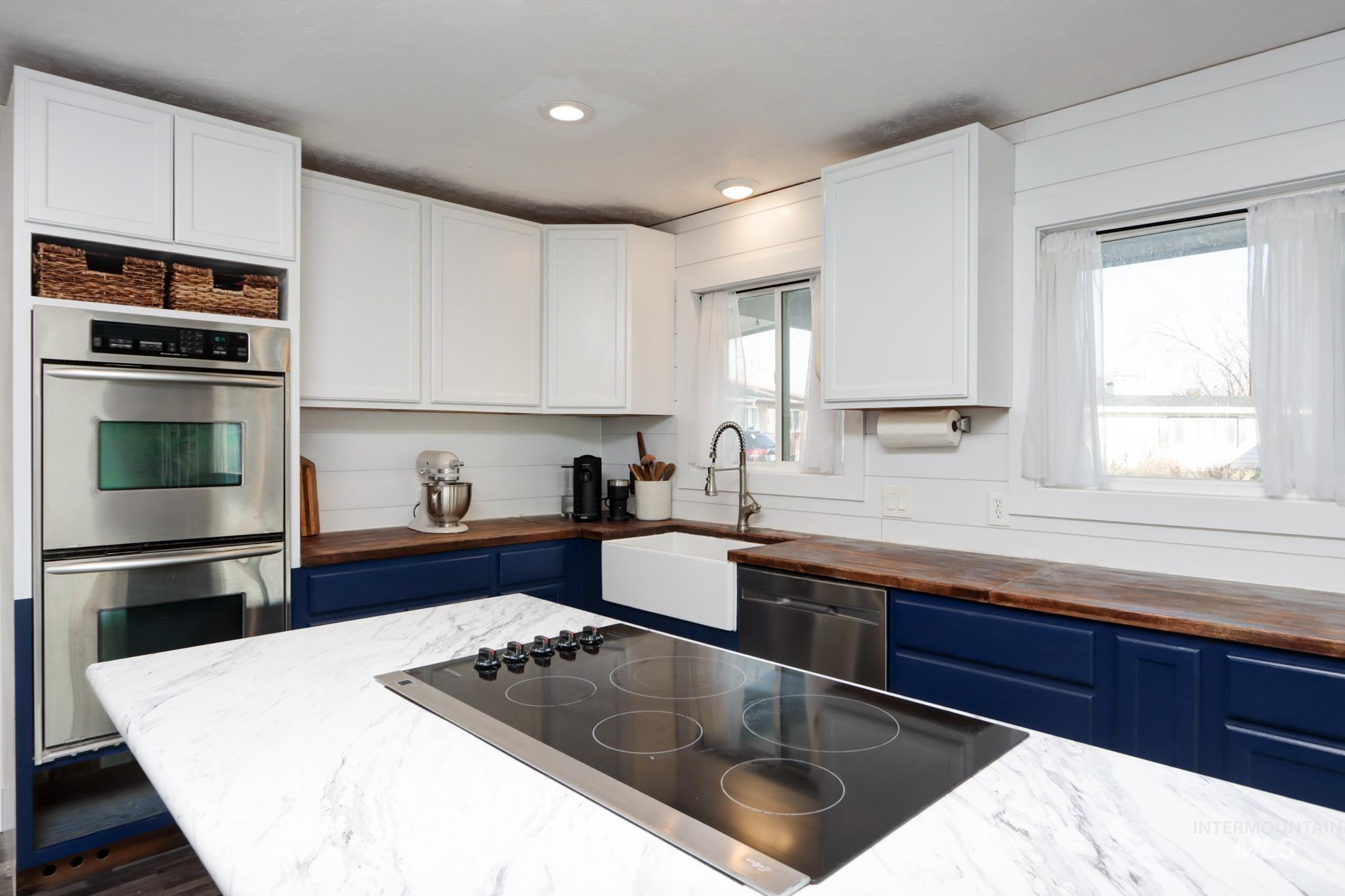 Kitchen with stainless steel appliances, butcher block counters, blue cabinets, white cabinetry, and recessed lighting