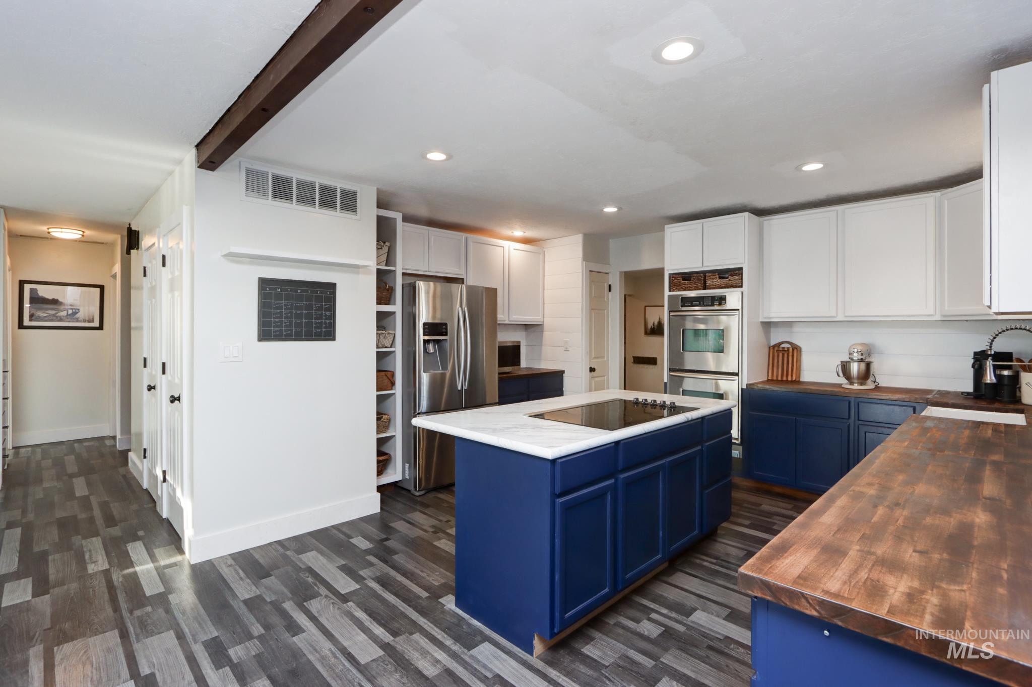 Kitchen with blue cabinets, white cabinets, stainless steel appliances, butcher block countertops, and dark wood-type flooring