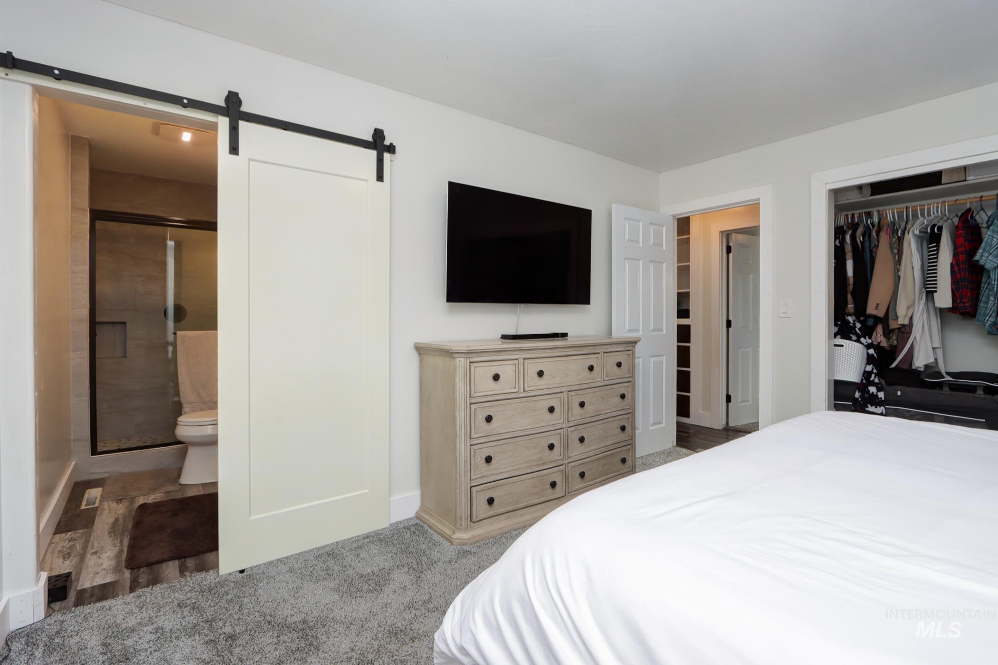 Bedroom with a barn door, a closet, ensuite bath, and light carpet