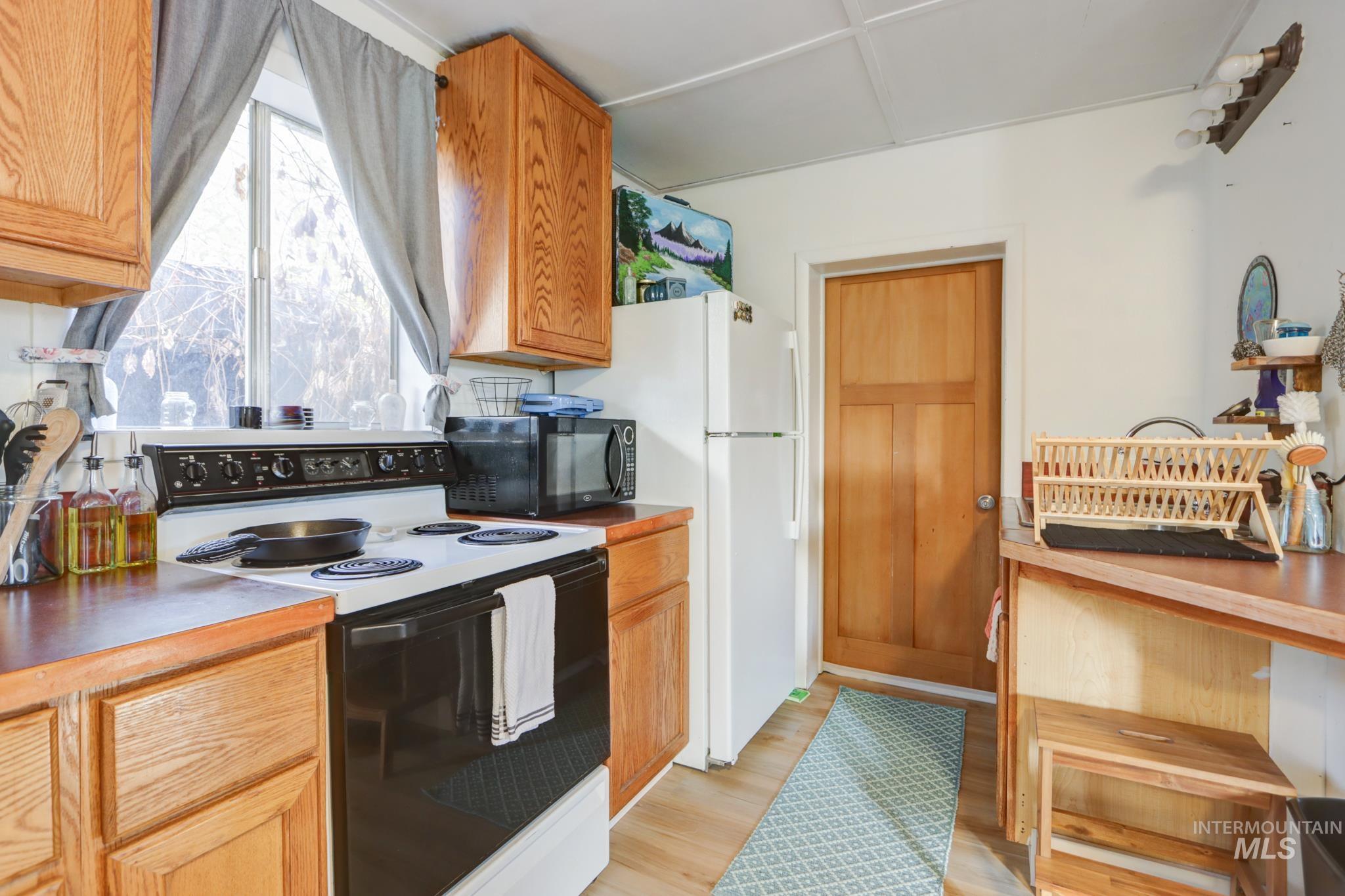 Kitchen featuring electric range oven, black microwave, light wood-style flooring, and brown cabinets