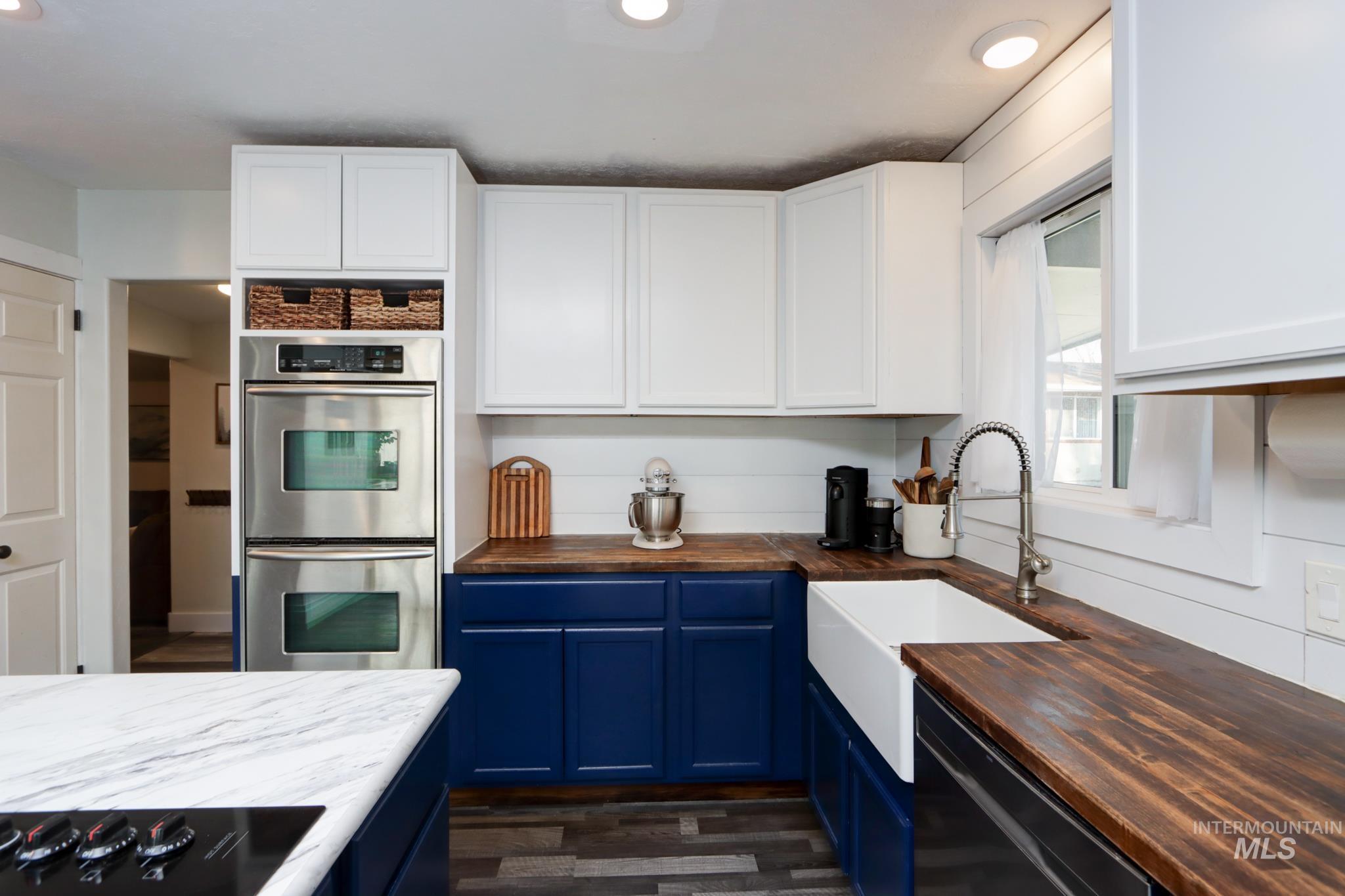 Kitchen featuring butcher block countertops, black appliances, blue cabinetry, dark wood finished floors, and white cabinetry