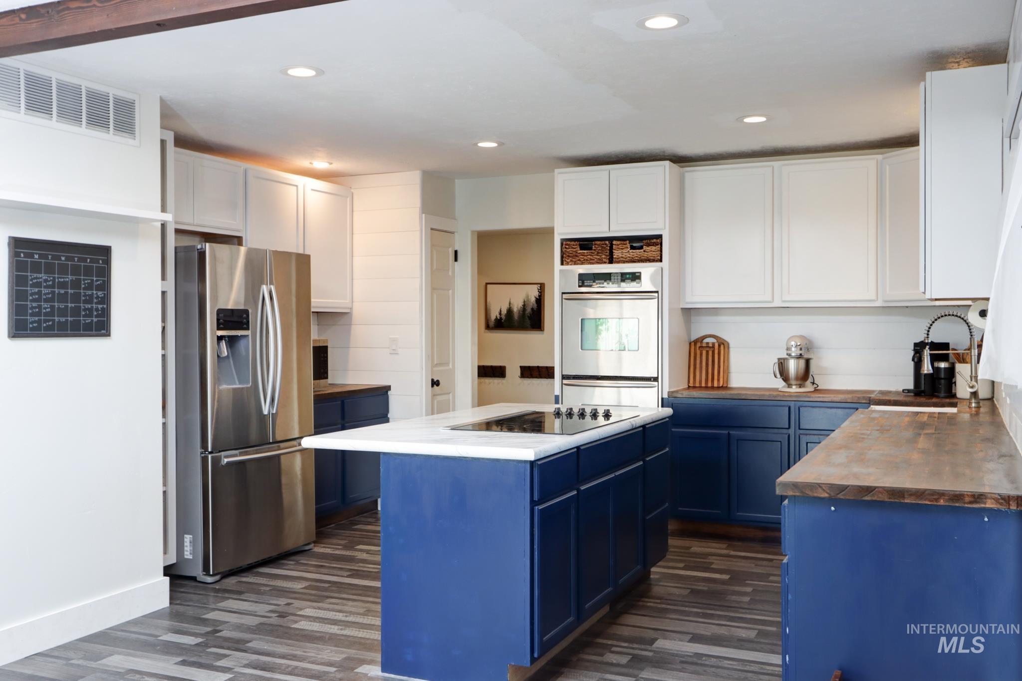 Kitchen with blue cabinets, stainless steel appliances, wooden counters, white cabinetry, and dark wood-style flooring