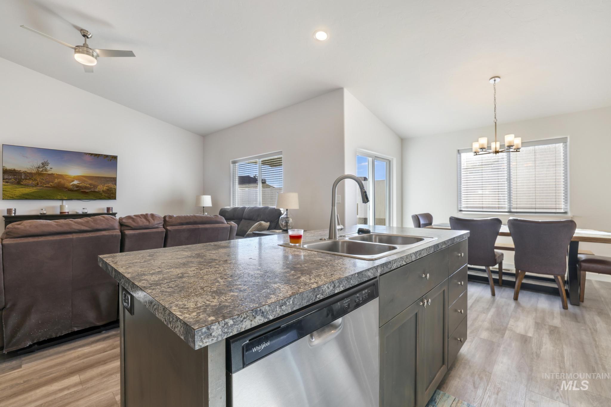 Kitchen with a center island with sink, stainless steel dishwasher, lofted ceiling, open floor plan, and light wood-style floors