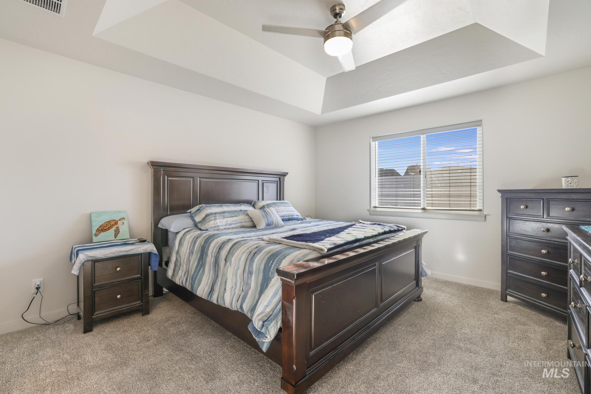 Bedroom featuring a raised ceiling, light colored carpet, and a ceiling fan