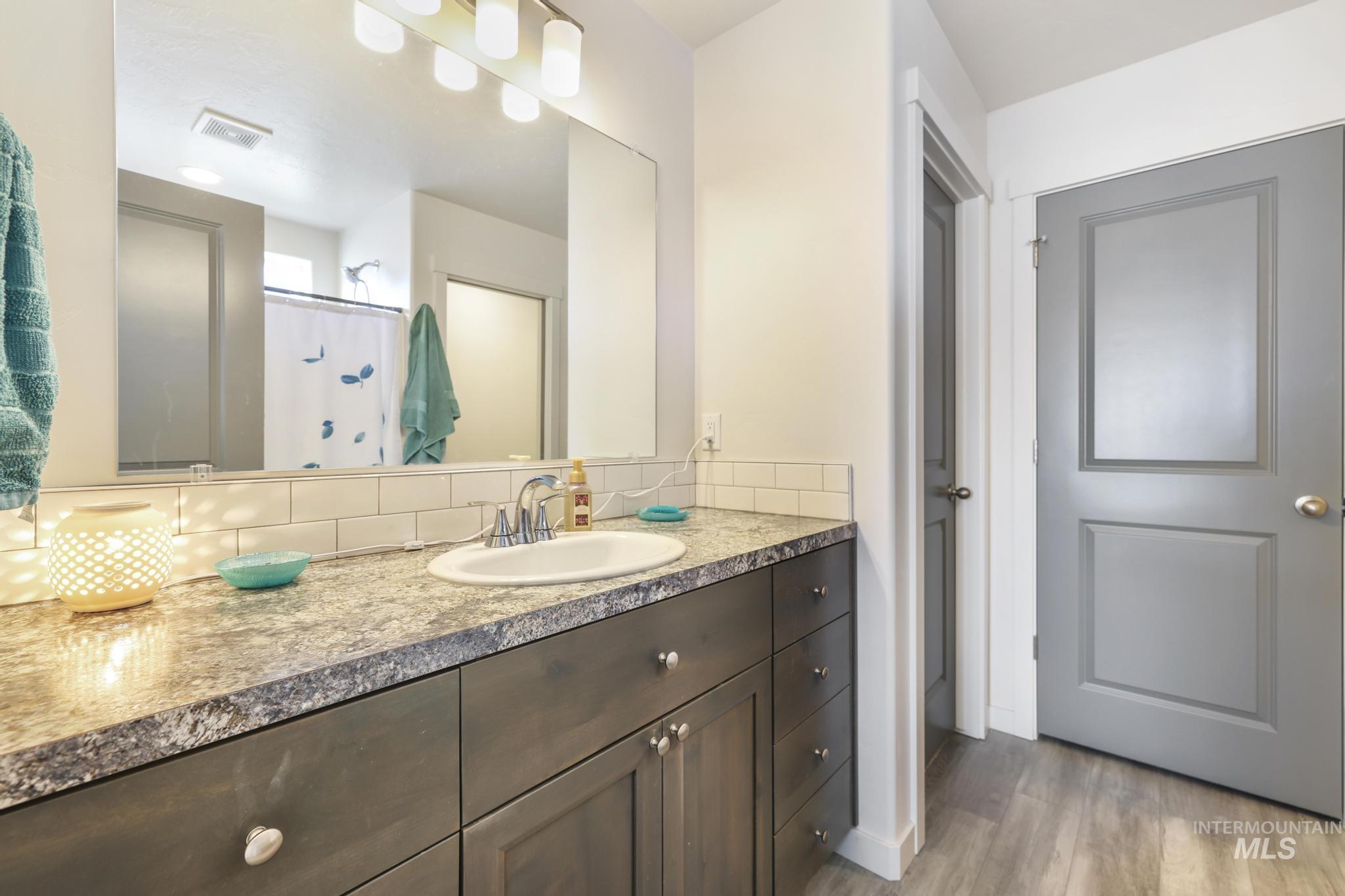 Bathroom featuring a shower with curtain, vanity, light wood-style flooring, and tasteful backsplash