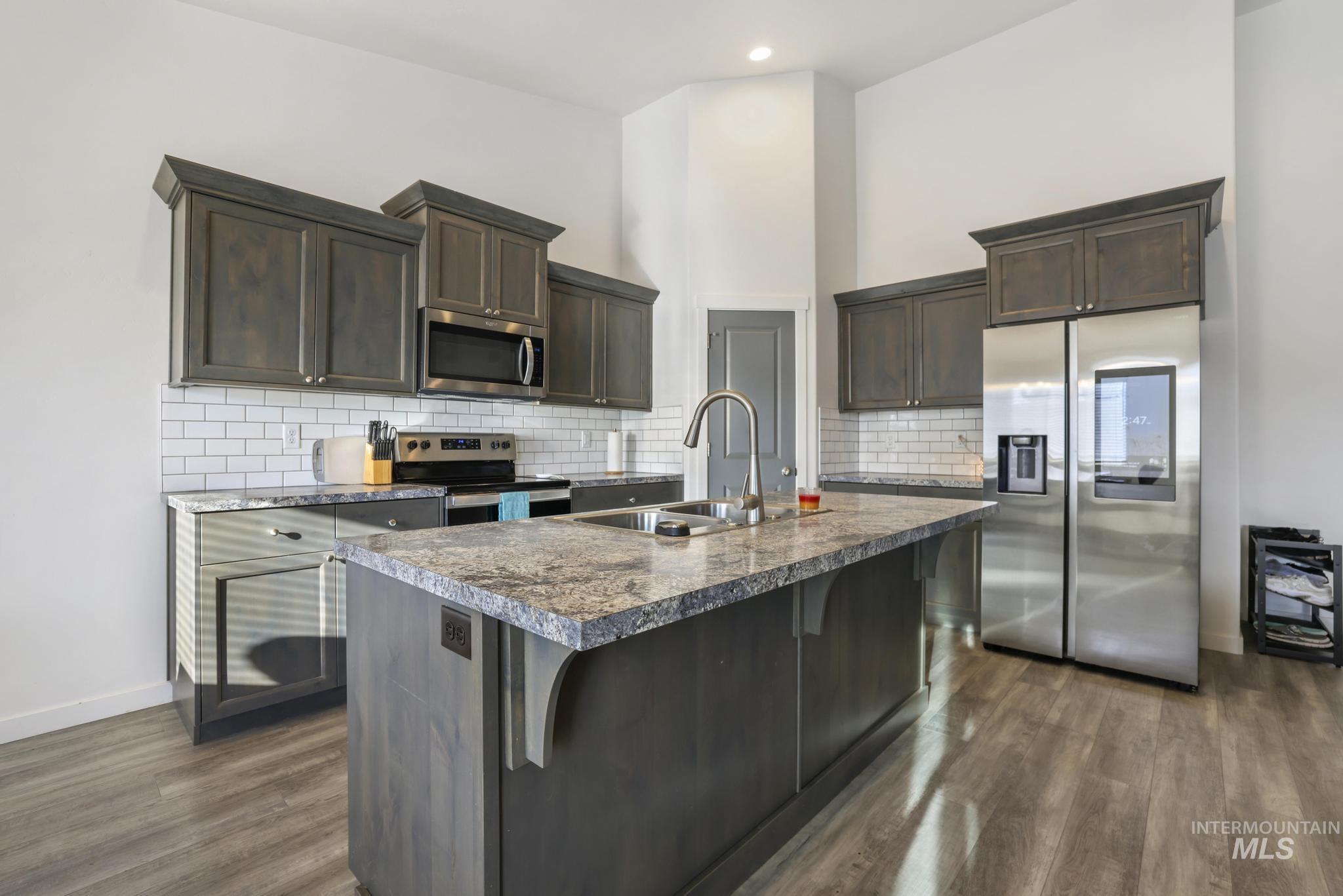 Kitchen with stainless steel appliances, dark brown cabinets, a kitchen island with sink, and backsplash