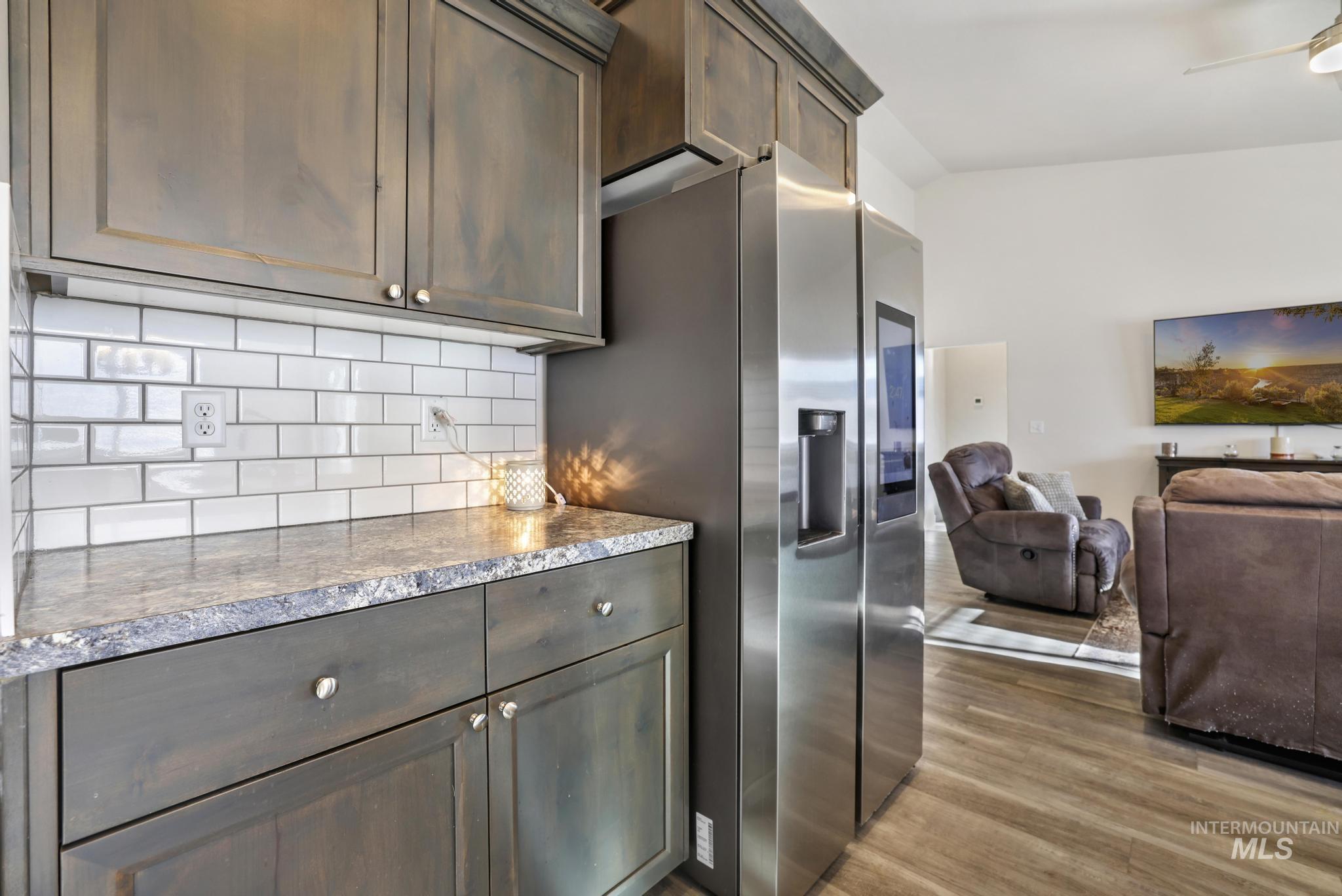 Kitchen featuring dark brown cabinets, backsplash, stainless steel fridge with ice dispenser, light wood finished floors, and open floor plan