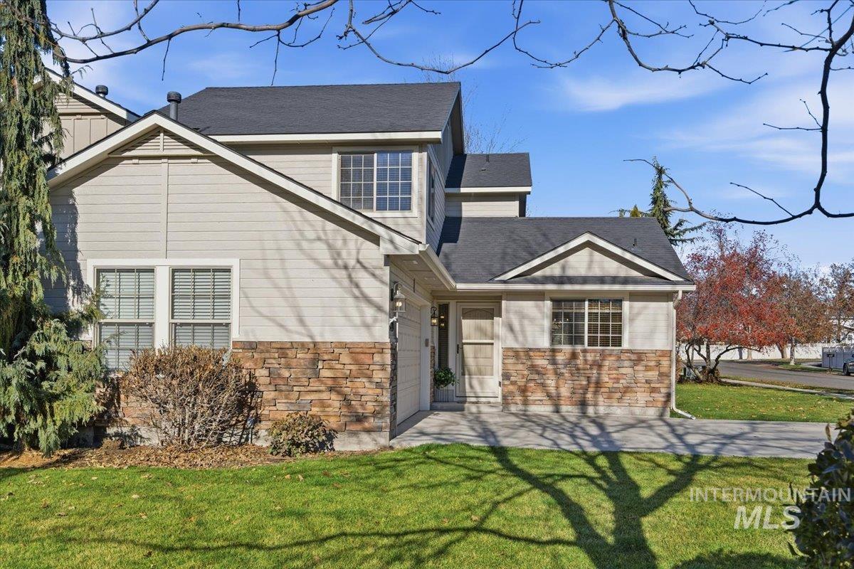 View of front of home featuring a front lawn, stone siding, and a shingled roof