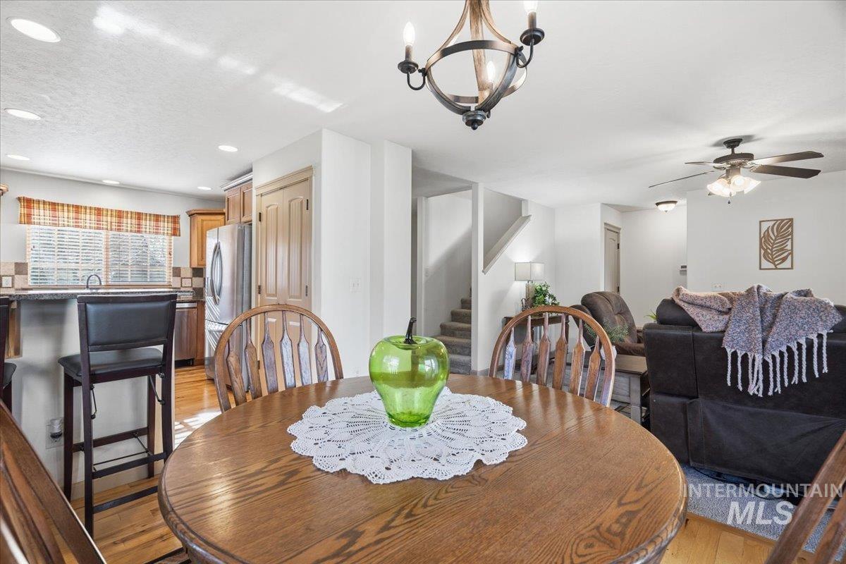 Dining room with light wood-type flooring, ceiling fan, a chandelier, a textured ceiling, and stairway