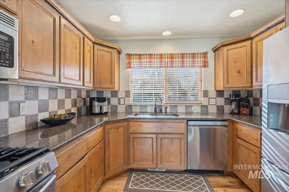 Kitchen featuring dark stone counters, stainless steel appliances, light wood-style flooring, and brown cabinetry