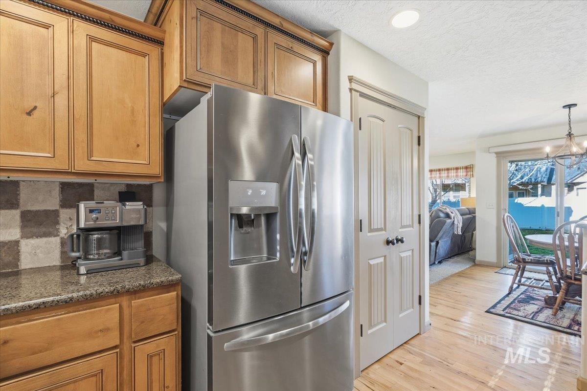 Kitchen featuring stainless steel fridge with ice dispenser, brown cabinets, a textured ceiling, dark stone counters, and a chandelier