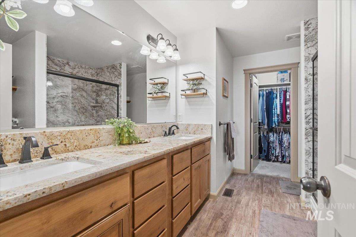 Bathroom with a marble finish shower, double vanity, a spacious closet, and light wood-type flooring