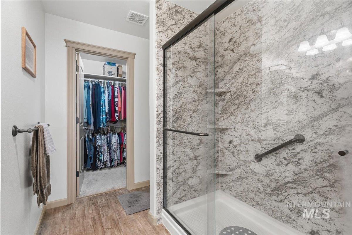 Bathroom with a spacious closet, a marble finish shower, and light wood-style flooring