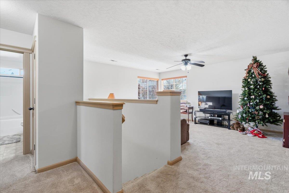 Corridor featuring an upstairs landing, light carpet, and a textured ceiling