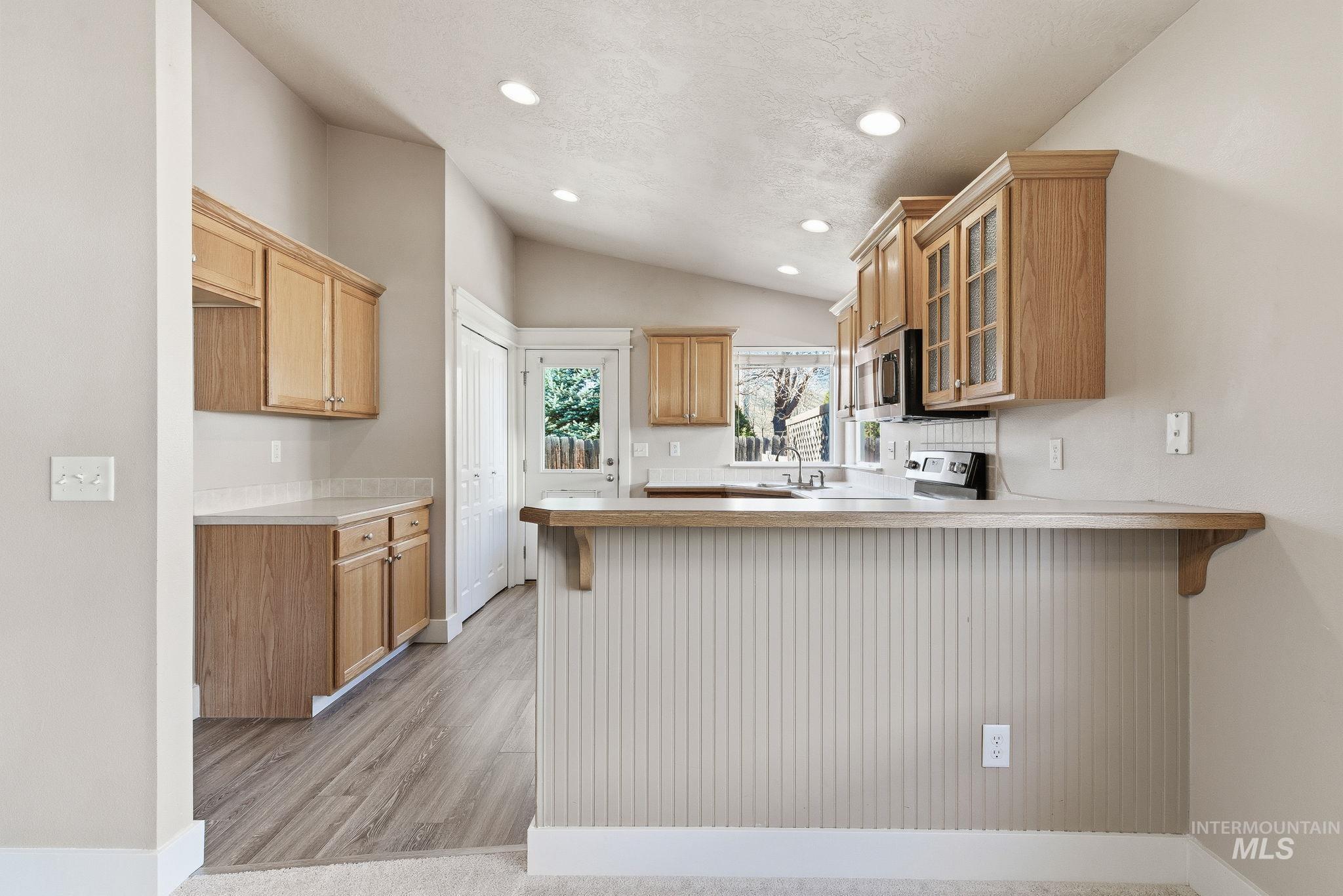 Kitchen featuring glass insert cabinets, a kitchen bar, light countertops, a peninsula, and vaulted ceiling