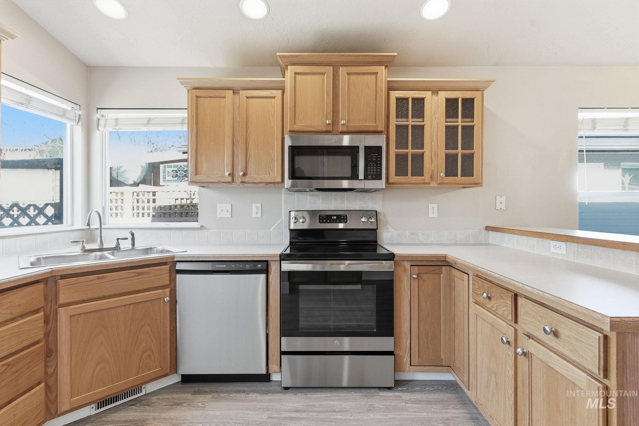 Kitchen featuring appliances with stainless steel finishes, light countertops, glass insert cabinets, light wood-style flooring, and recessed lighting