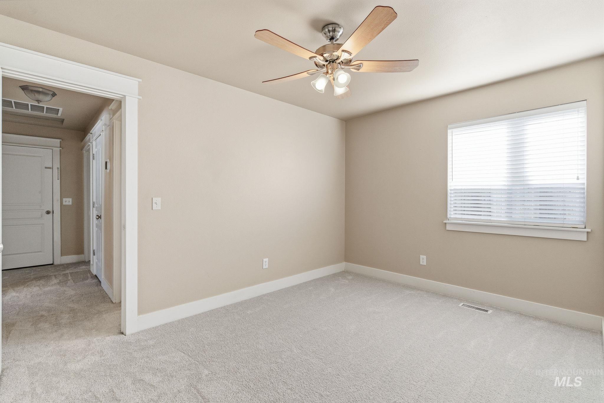 Empty room with light colored carpet and a ceiling fan