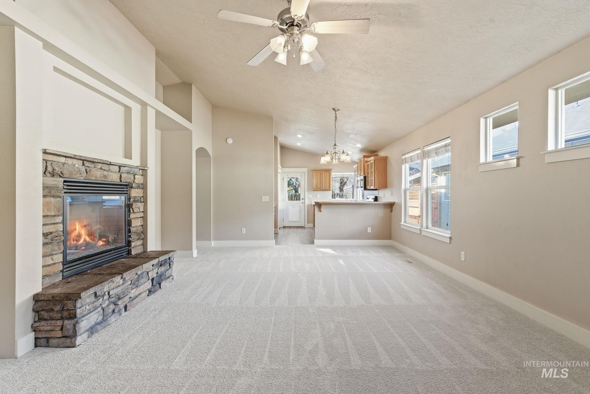 Unfurnished living room with lofted ceiling, light carpet, a fireplace, a ceiling fan, and a chandelier