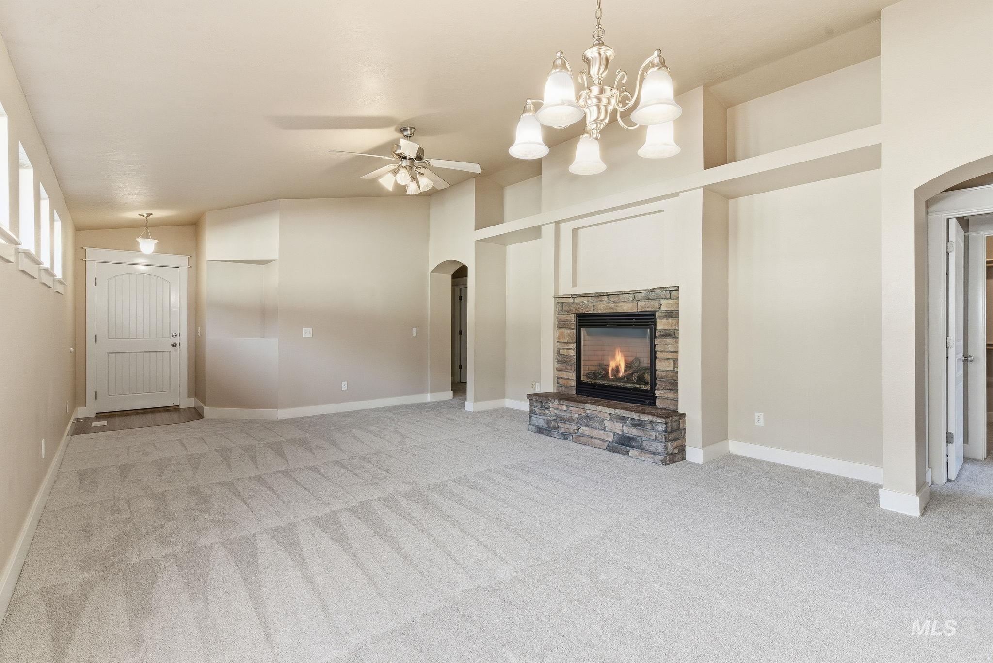 Unfurnished living room with arched walkways, light carpet, ceiling fan, and vaulted ceiling