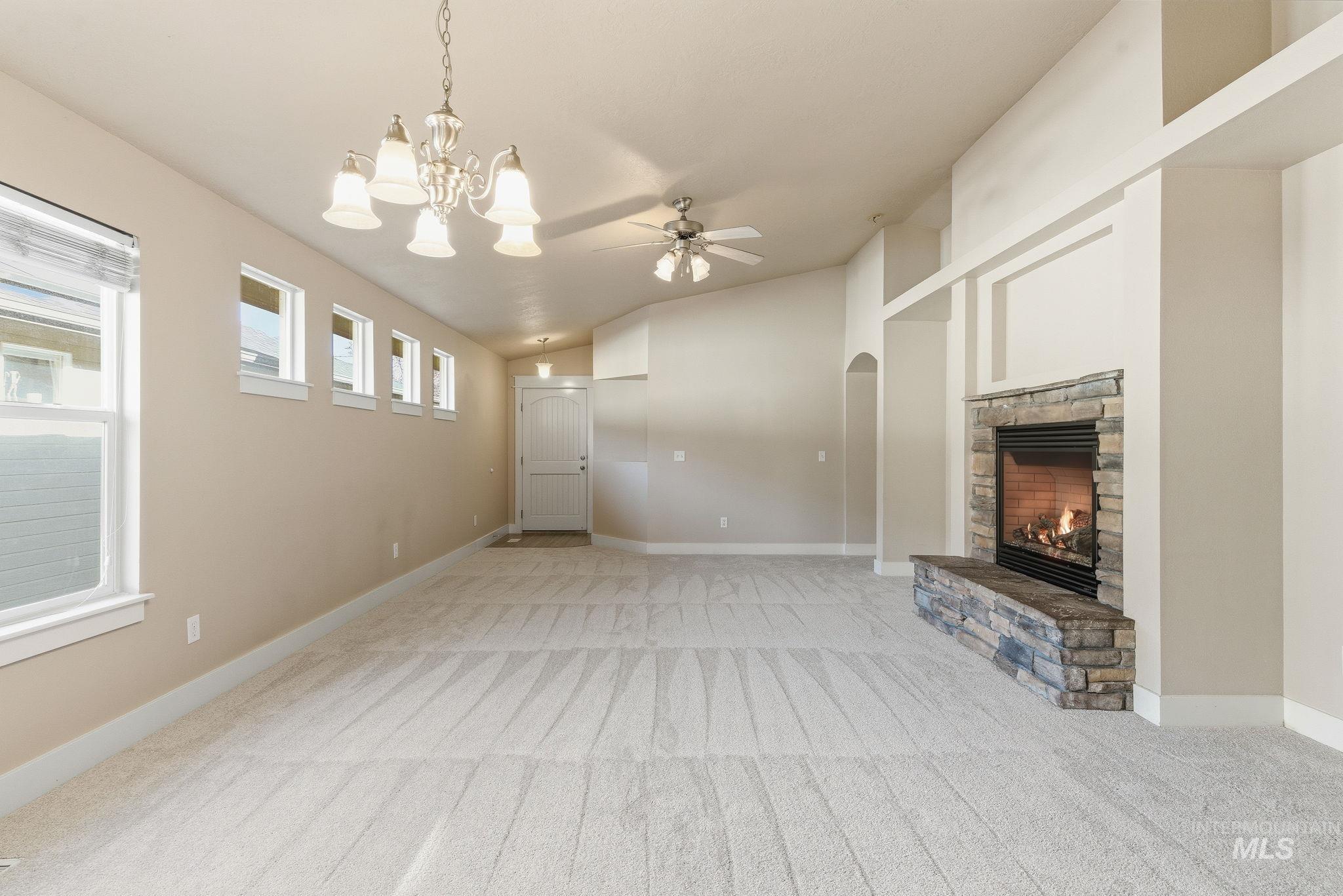 Unfurnished living room with a fireplace, lofted ceiling, light colored carpet, a ceiling fan, and arched walkways