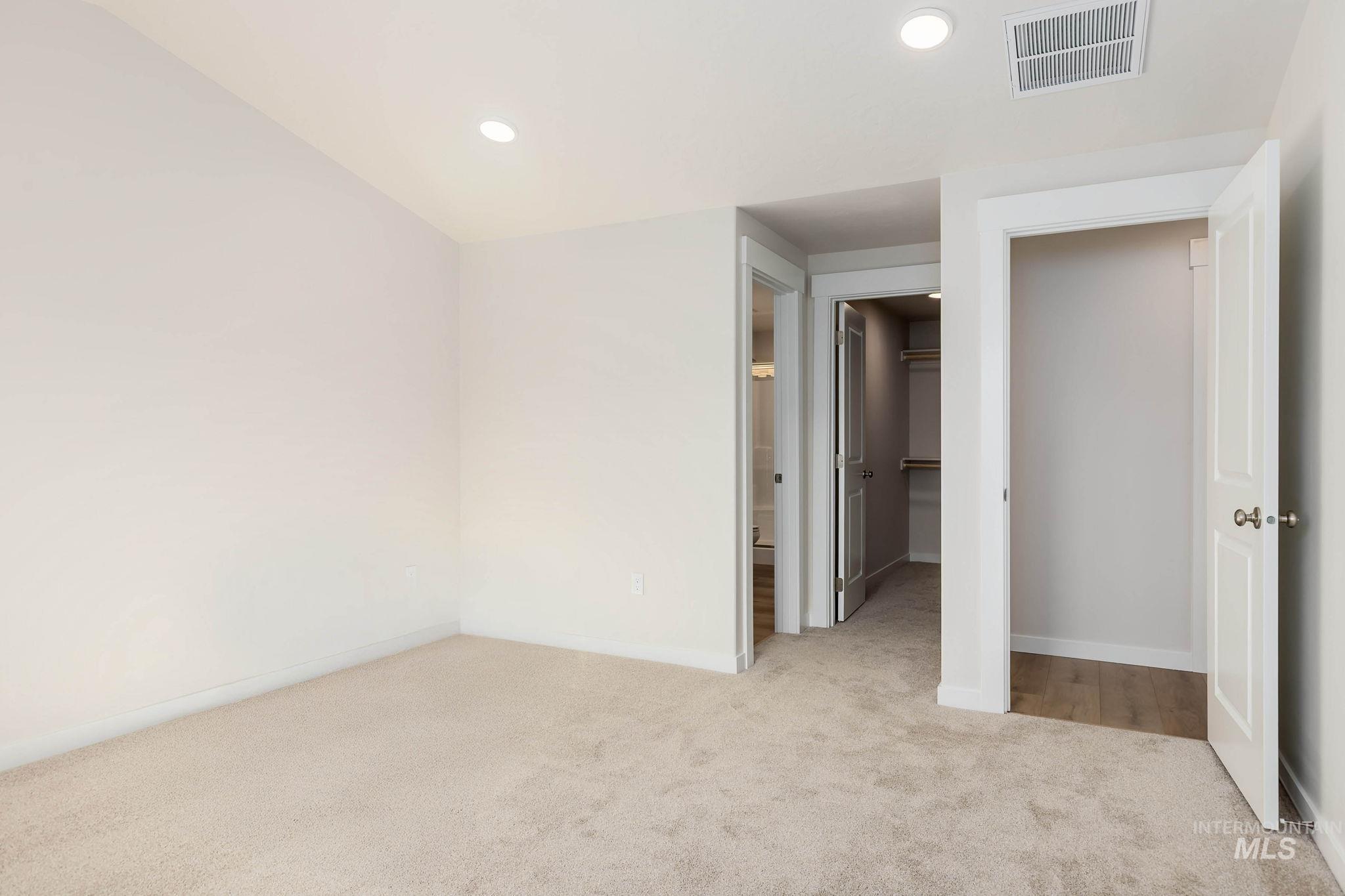 Unfurnished bedroom featuring a walk in closet, light colored carpet, recessed lighting, and connected bathroom
