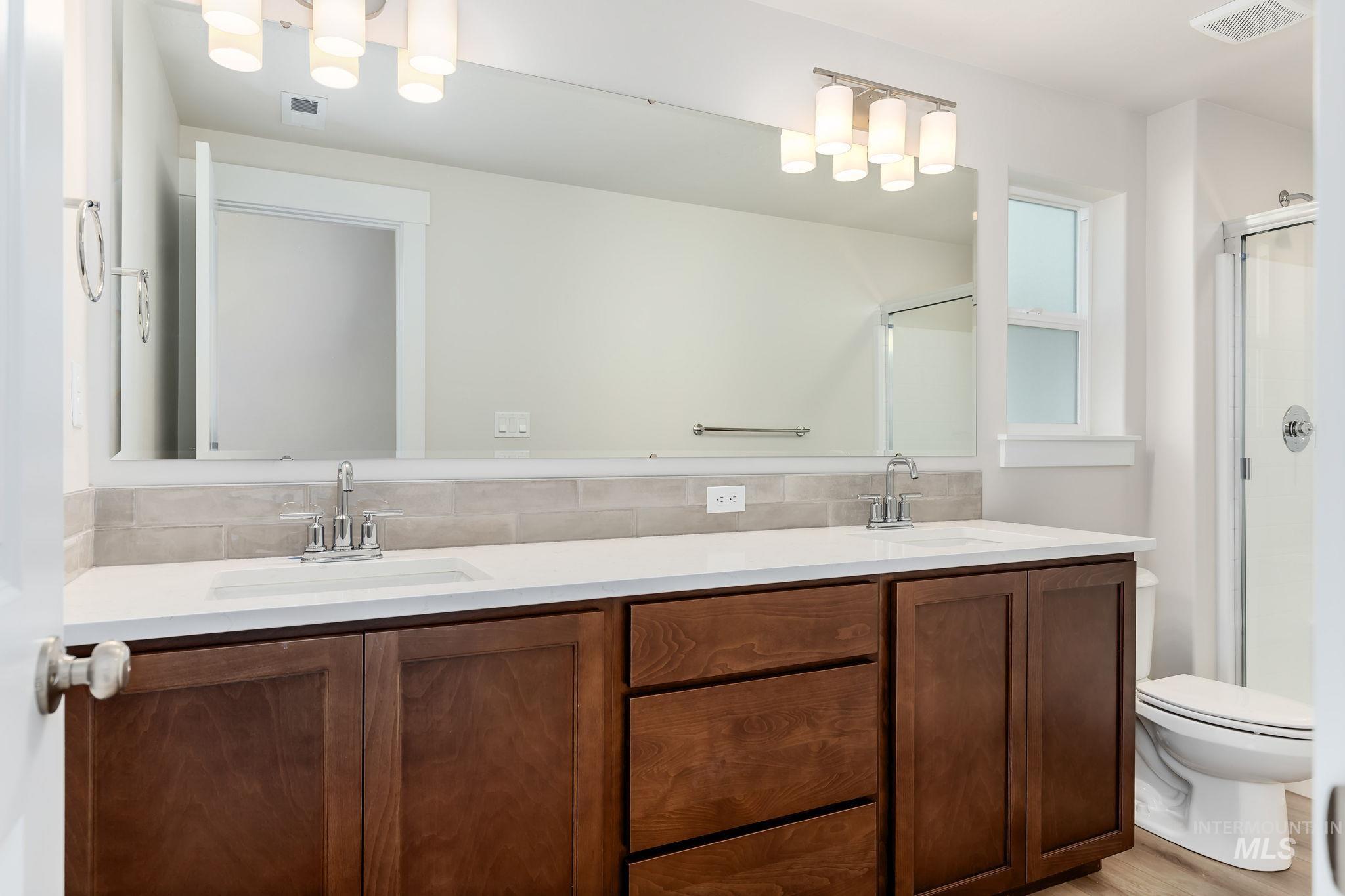 Bathroom featuring double vanity, a stall shower, and backsplash
