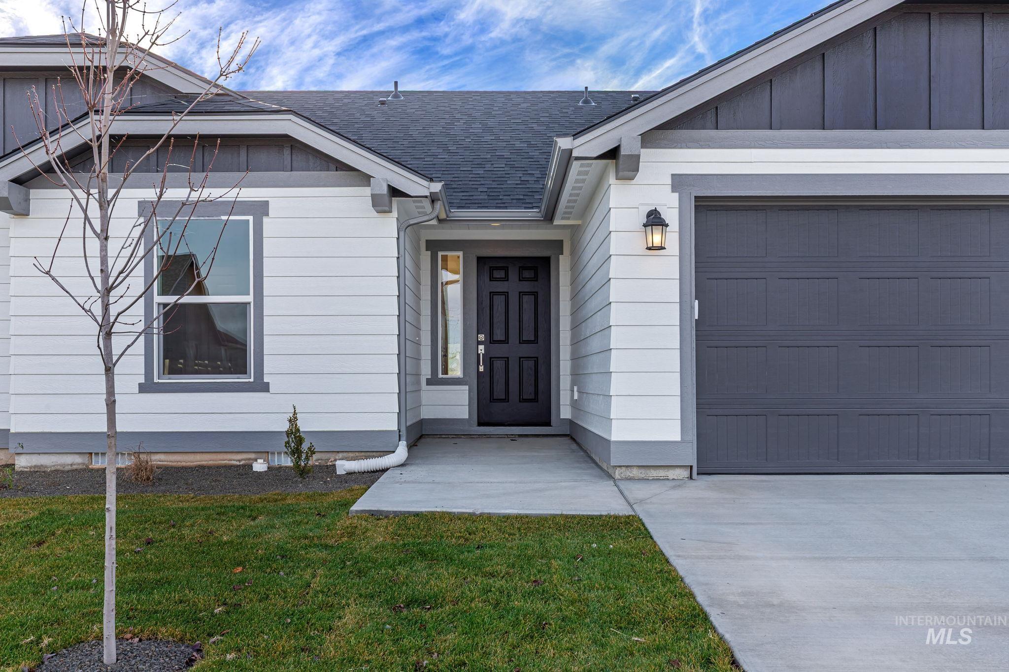 Entrance to property featuring an attached garage, a shingled roof, and a lawn