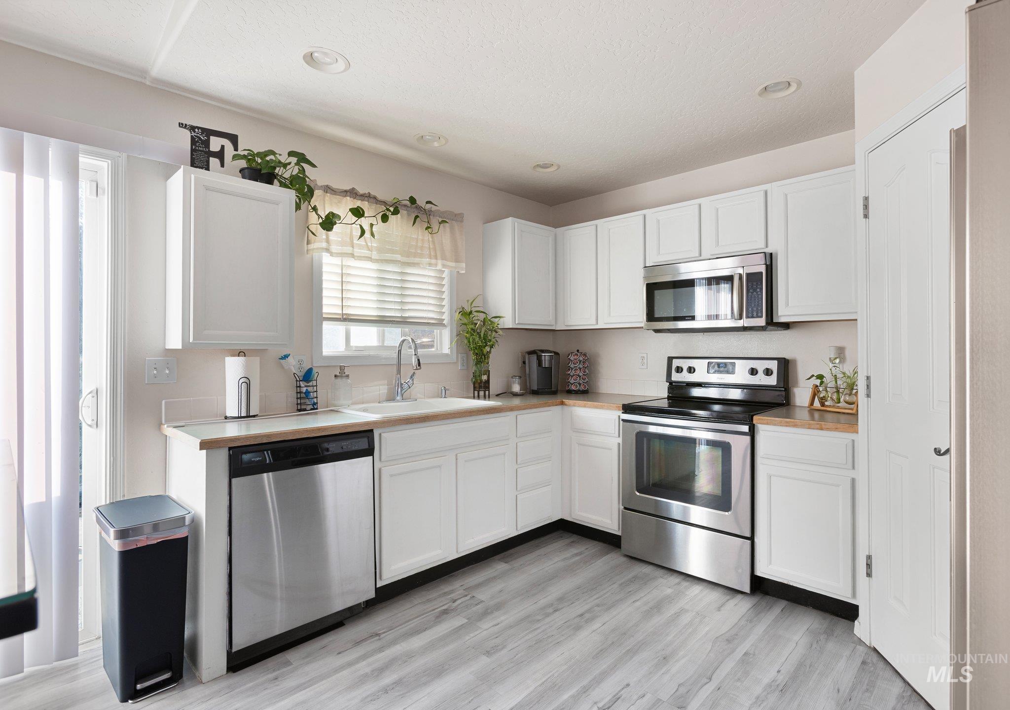 Kitchen featuring appliances with stainless steel finishes, white cabinetry, light countertops, light wood-style floors, and a textured ceiling