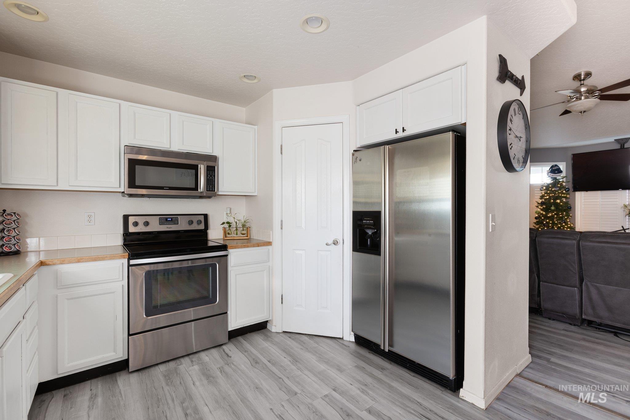 Kitchen featuring stainless steel appliances, light countertops, white cabinetry, ceiling fan, and light wood finished floors