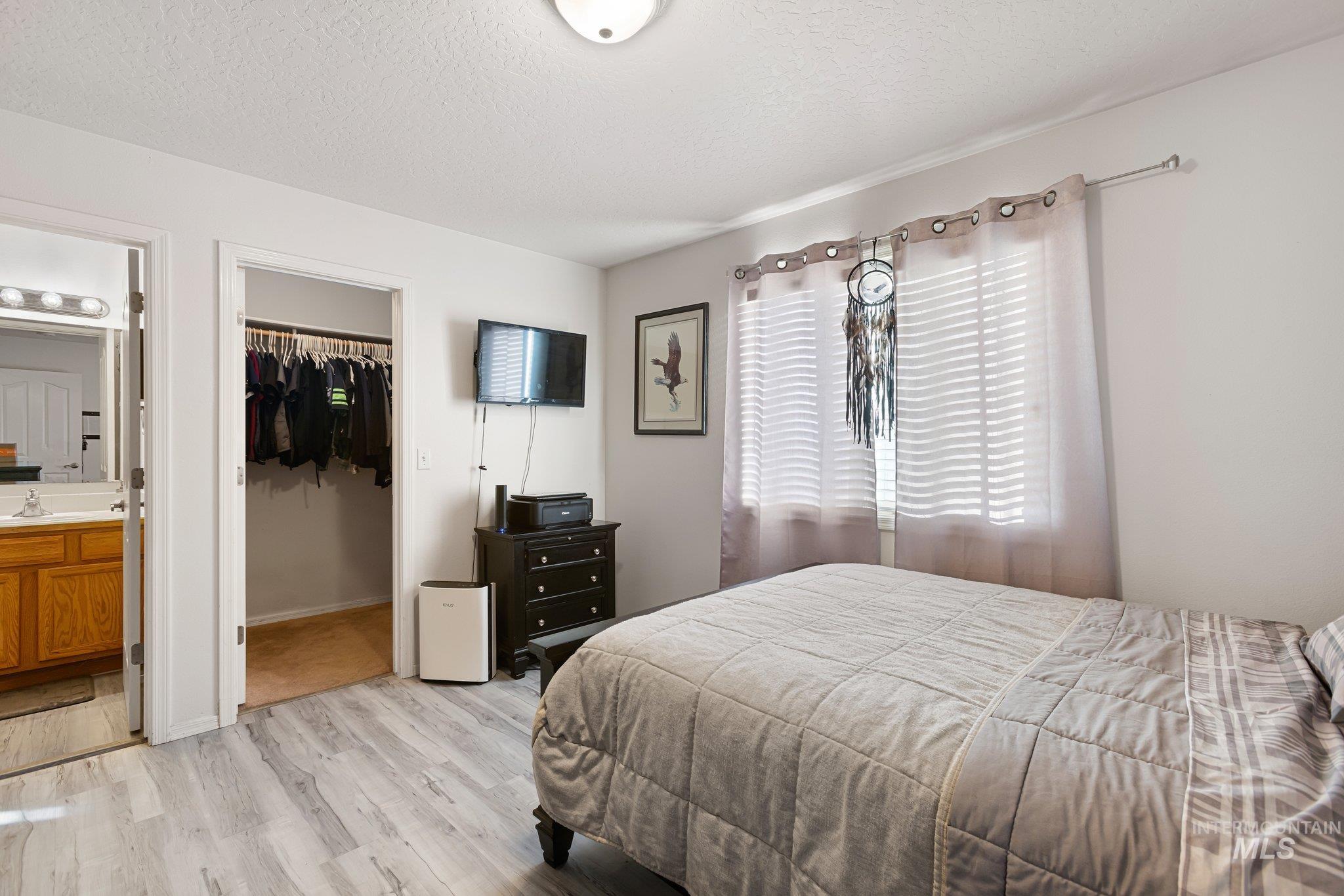 Bedroom featuring light wood-style flooring, a textured ceiling, a spacious closet, and connected bathroom