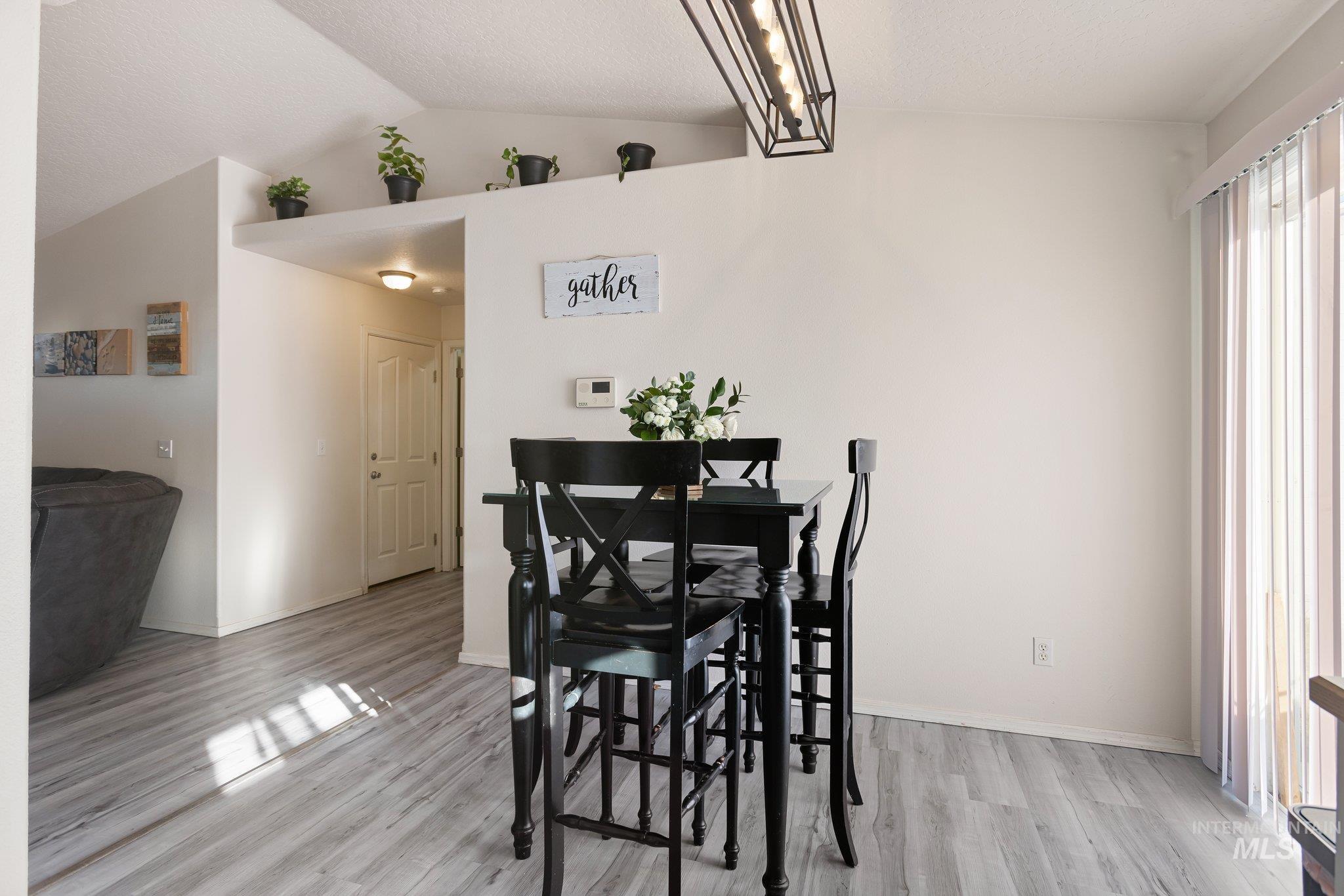 Dining area featuring vaulted ceiling, light wood finished floors, and a textured ceiling