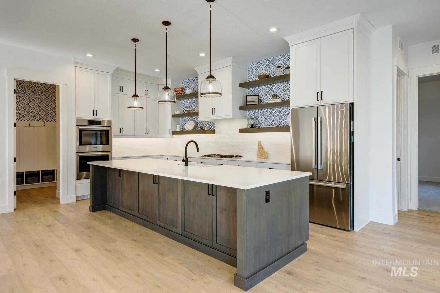 Kitchen featuring open shelves, stainless steel appliances, white cabinets, decorative light fixtures, and a center island with sink