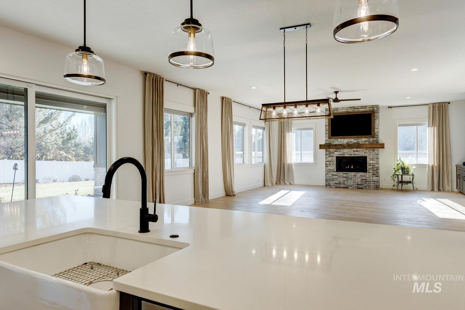 Kitchen with open floor plan, hanging light fixtures, light stone counters, light wood-style flooring, and a brick fireplace