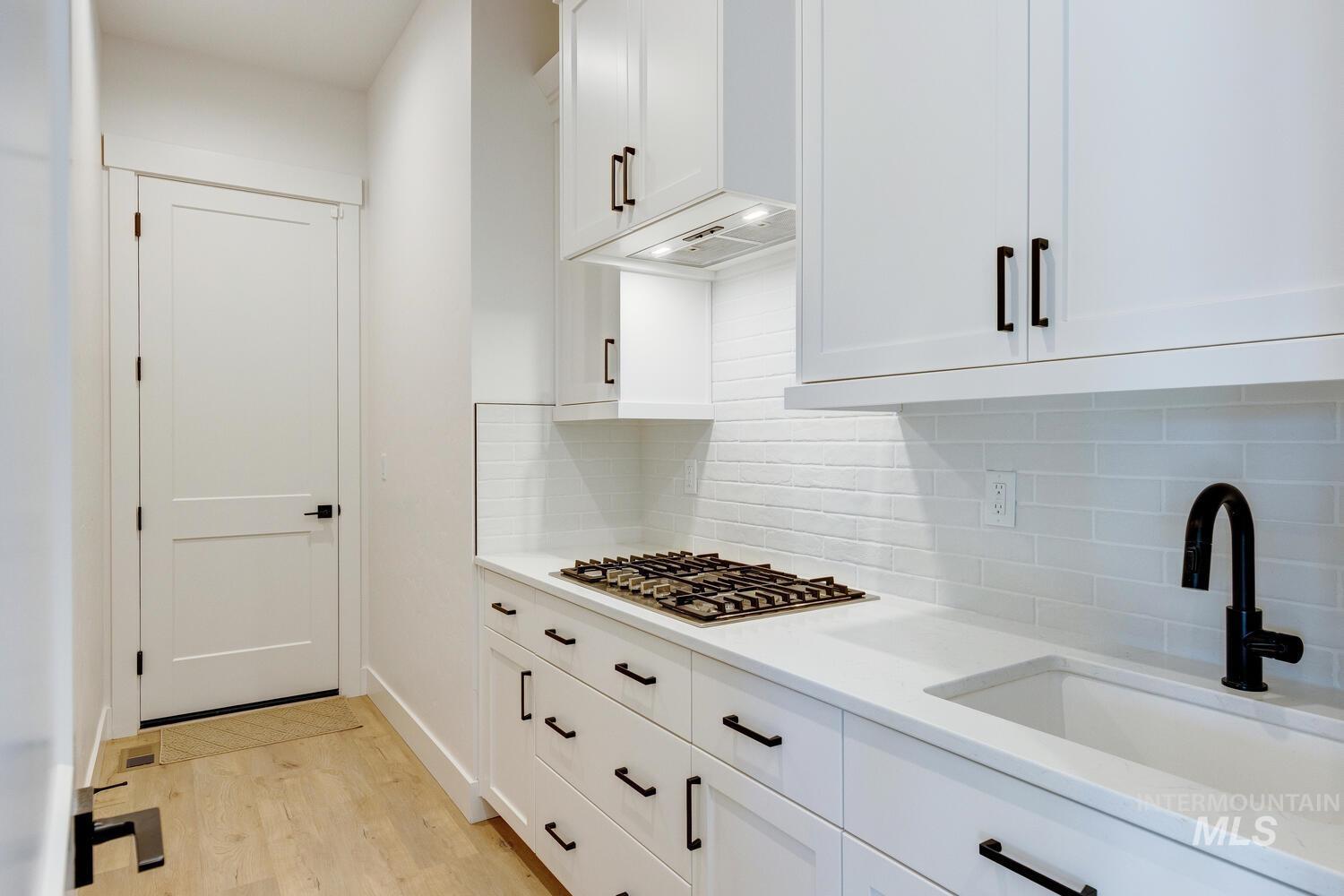 Kitchen with white cabinets, light wood-style flooring, decorative backsplash, and light stone counters