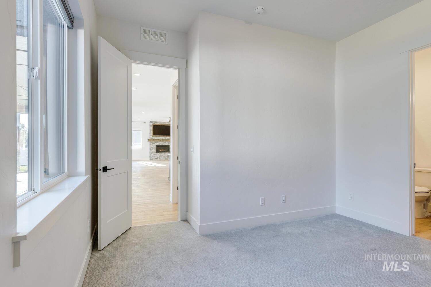 Unfurnished bedroom with light colored carpet, a stone fireplace, and ensuite bathroom