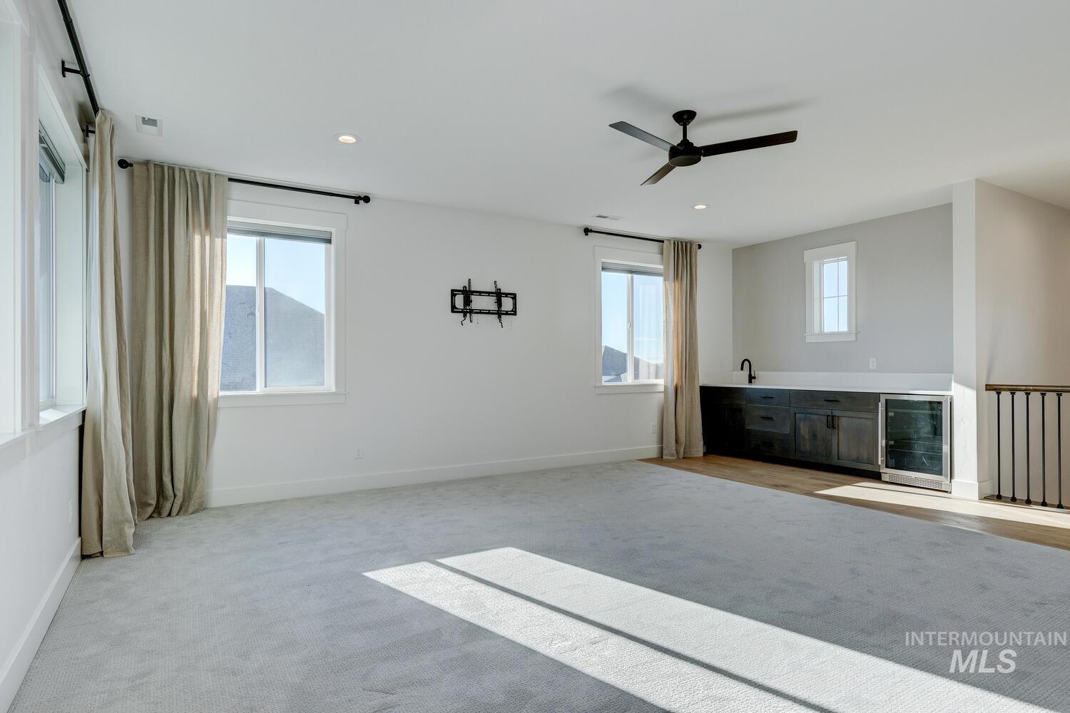 Unfurnished living room with beverage cooler, light carpet, healthy amount of natural light, ceiling fan, and recessed lighting