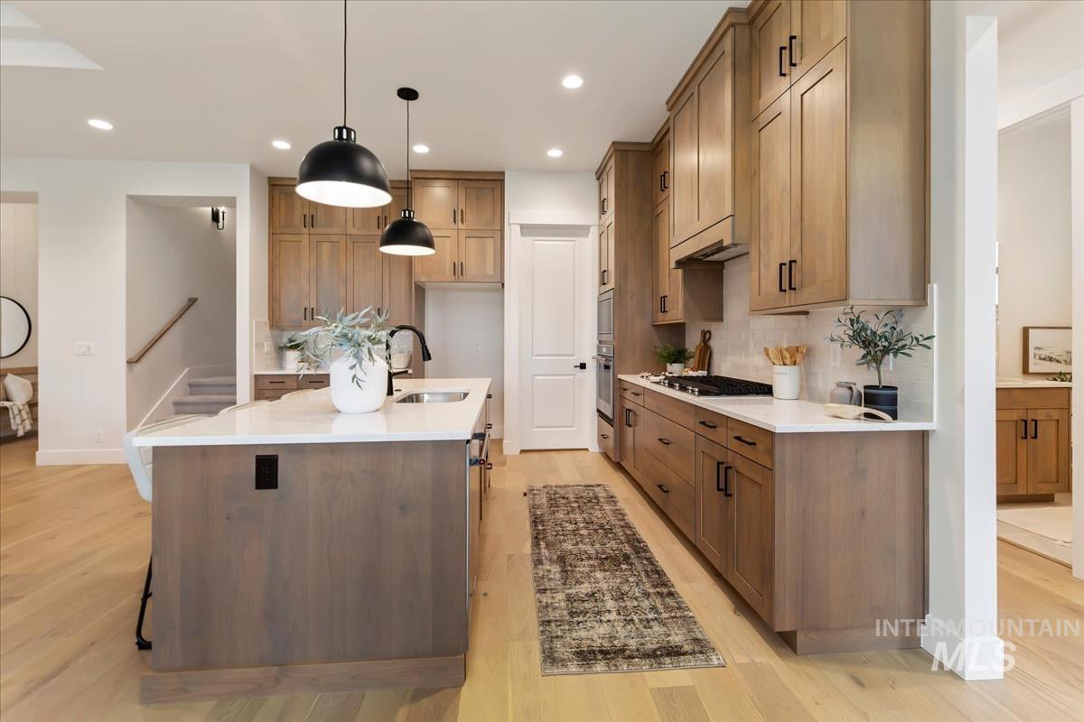 Kitchen featuring light stone counters, hanging light fixtures, brown cabinets, a center island with sink, and recessed lighting