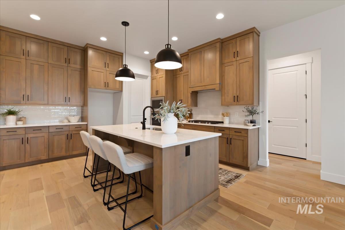 Kitchen with brown cabinetry, a kitchen breakfast bar, tasteful backsplash, pendant lighting, and recessed lighting