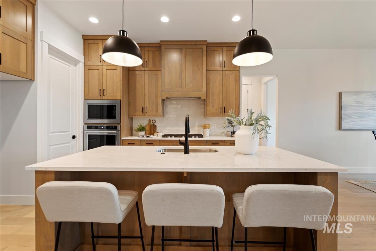 Kitchen featuring light wood-type flooring, a breakfast bar, brown cabinetry, hanging light fixtures, and recessed lighting
