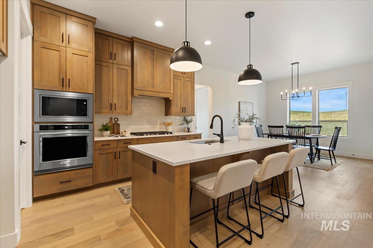 Kitchen with brown cabinets, appliances with stainless steel finishes, pendant lighting, decorative backsplash, and a kitchen island with sink