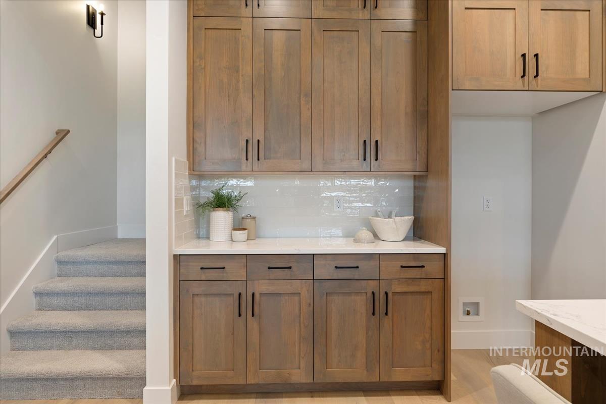 Bar area featuring decorative backsplash, brown cabinets, light stone countertops, and stairs