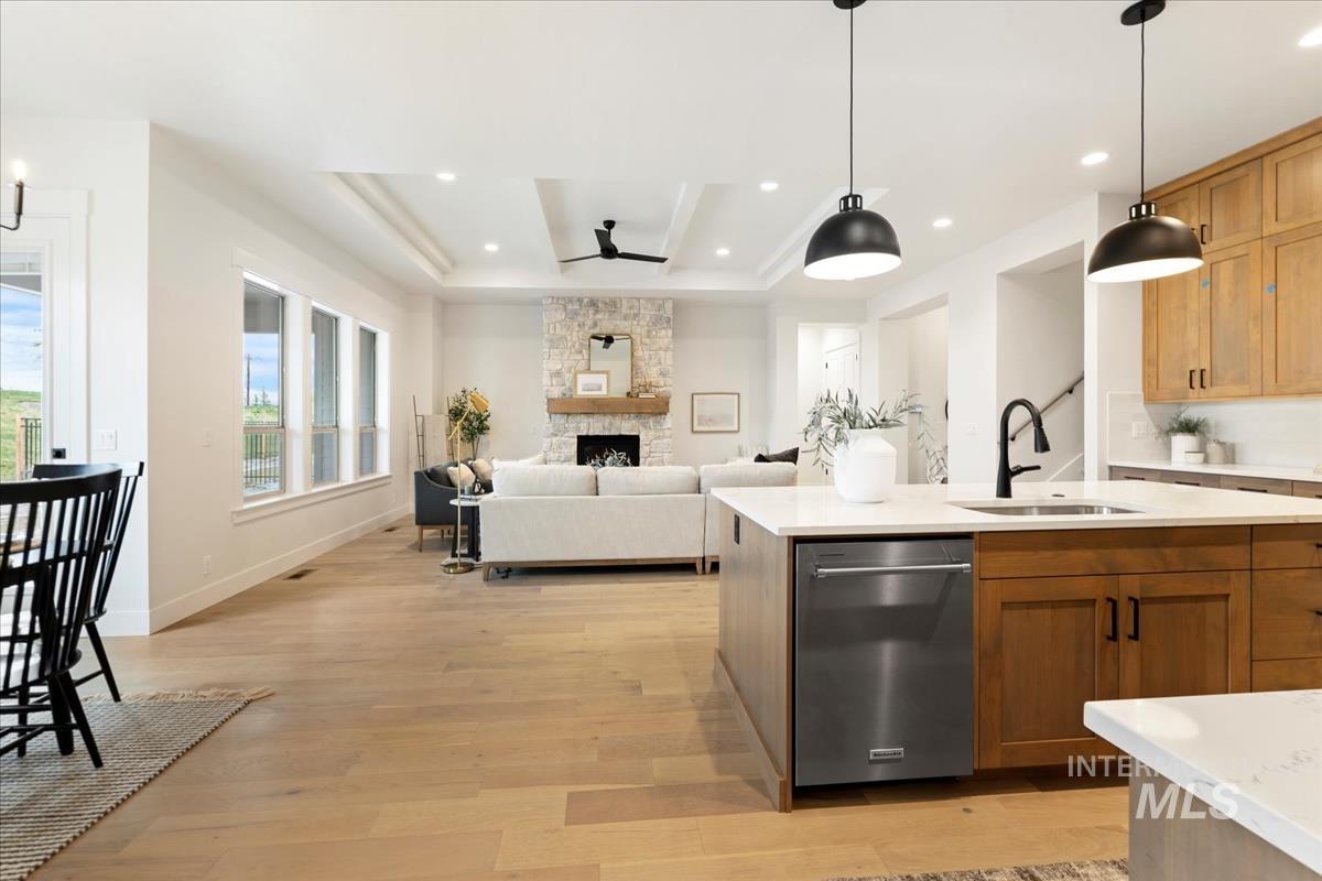 Kitchen with dishwasher, decorative light fixtures, light wood-type flooring, a ceiling fan, and a stone fireplace